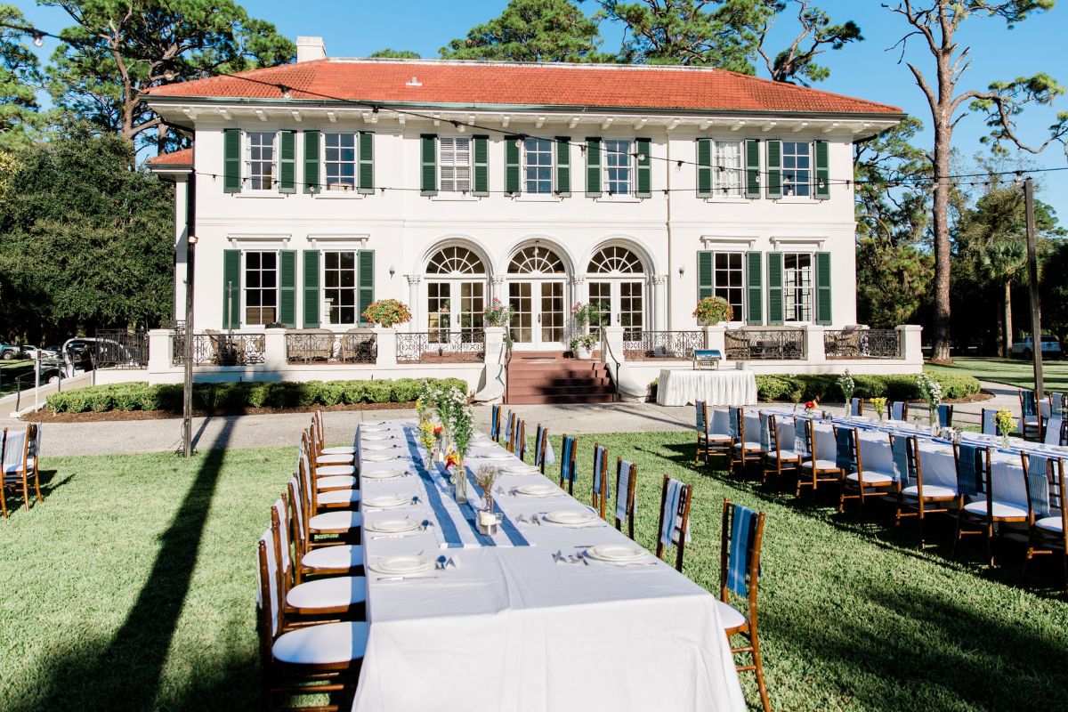 a long table set for a dinner party outside of a large white house