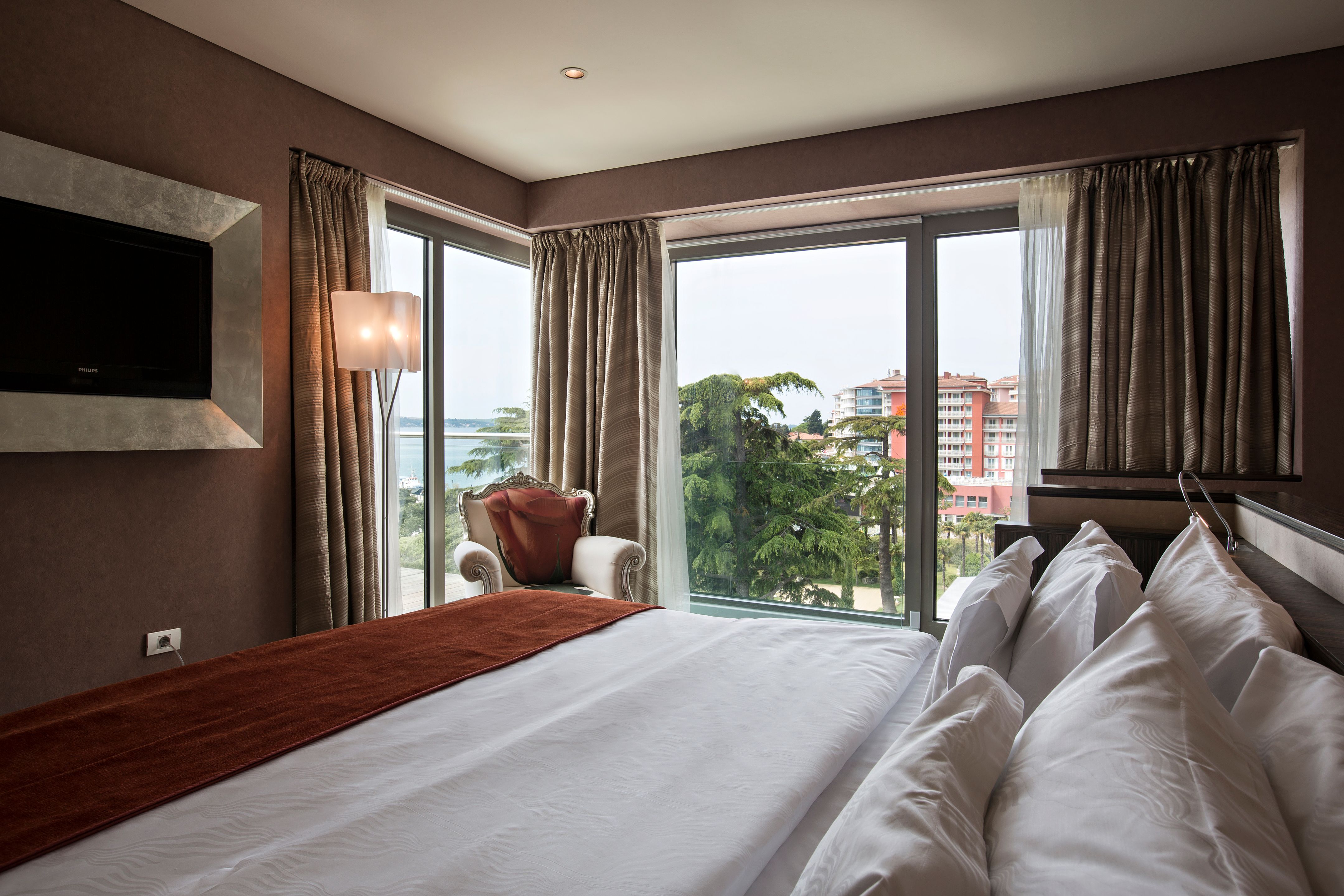 a bed with white sheets and pillows in a room with a large window