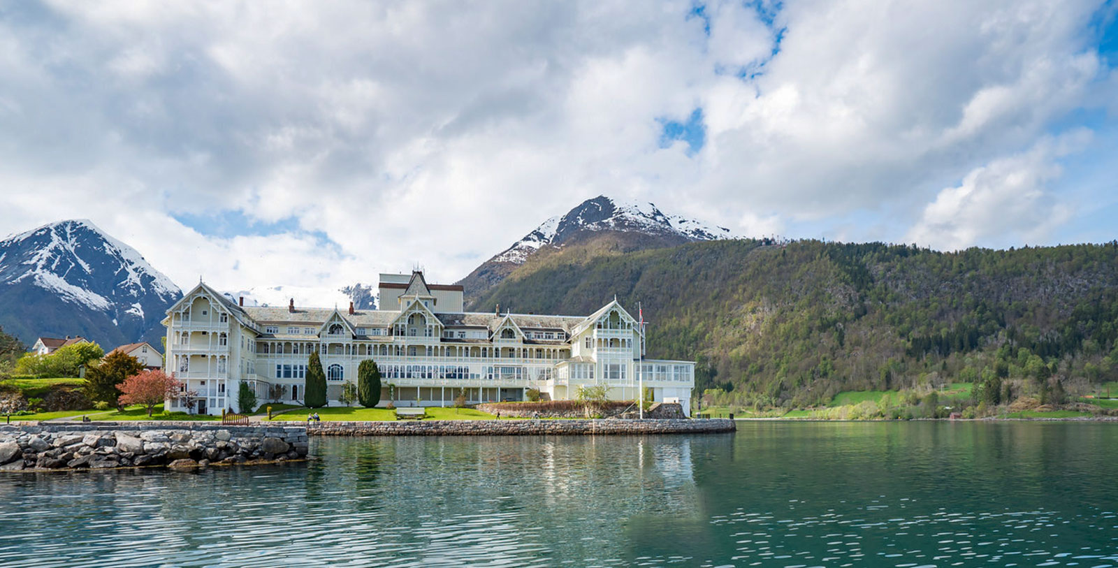 a large white building with a large body of water and mountains in the background