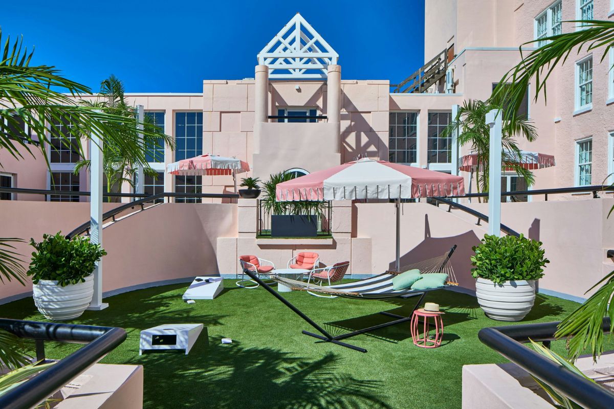 a hammocks on a green lawn with pink umbrellas and palm trees