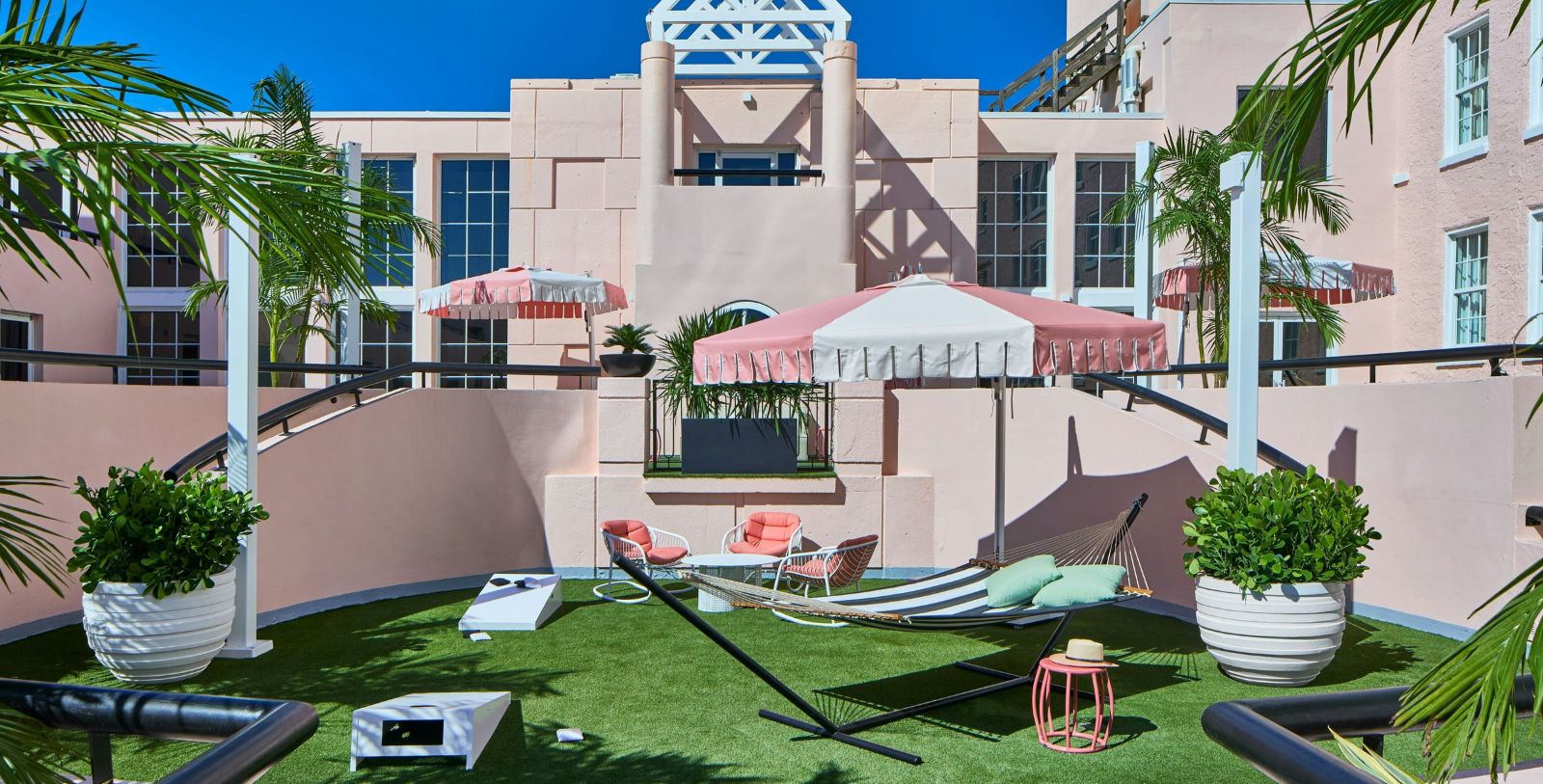 a hammock on a lawn with pink umbrellas and palm trees