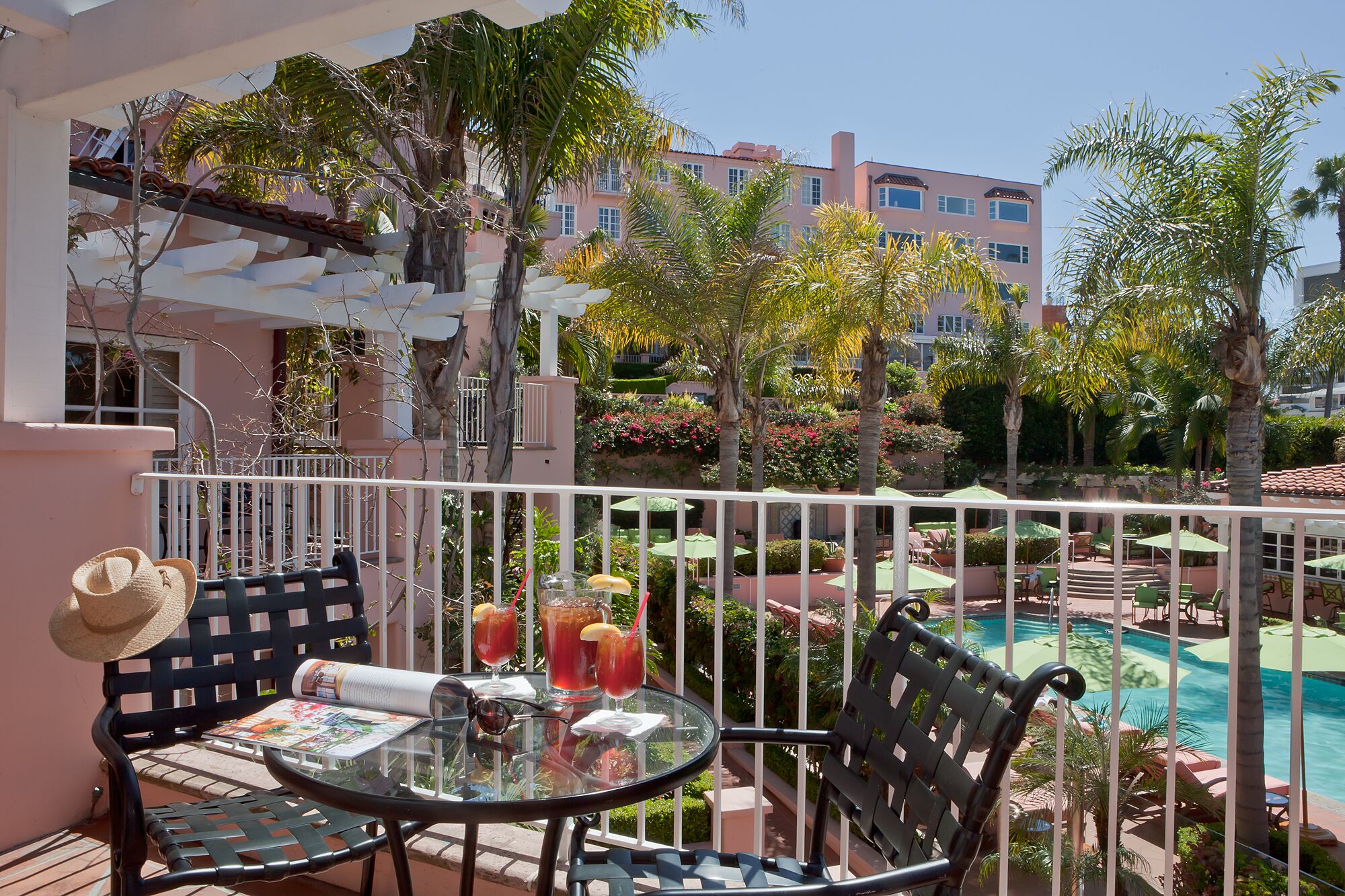 a table with drinks on it and chairs on a balcony with palm trees and buildings