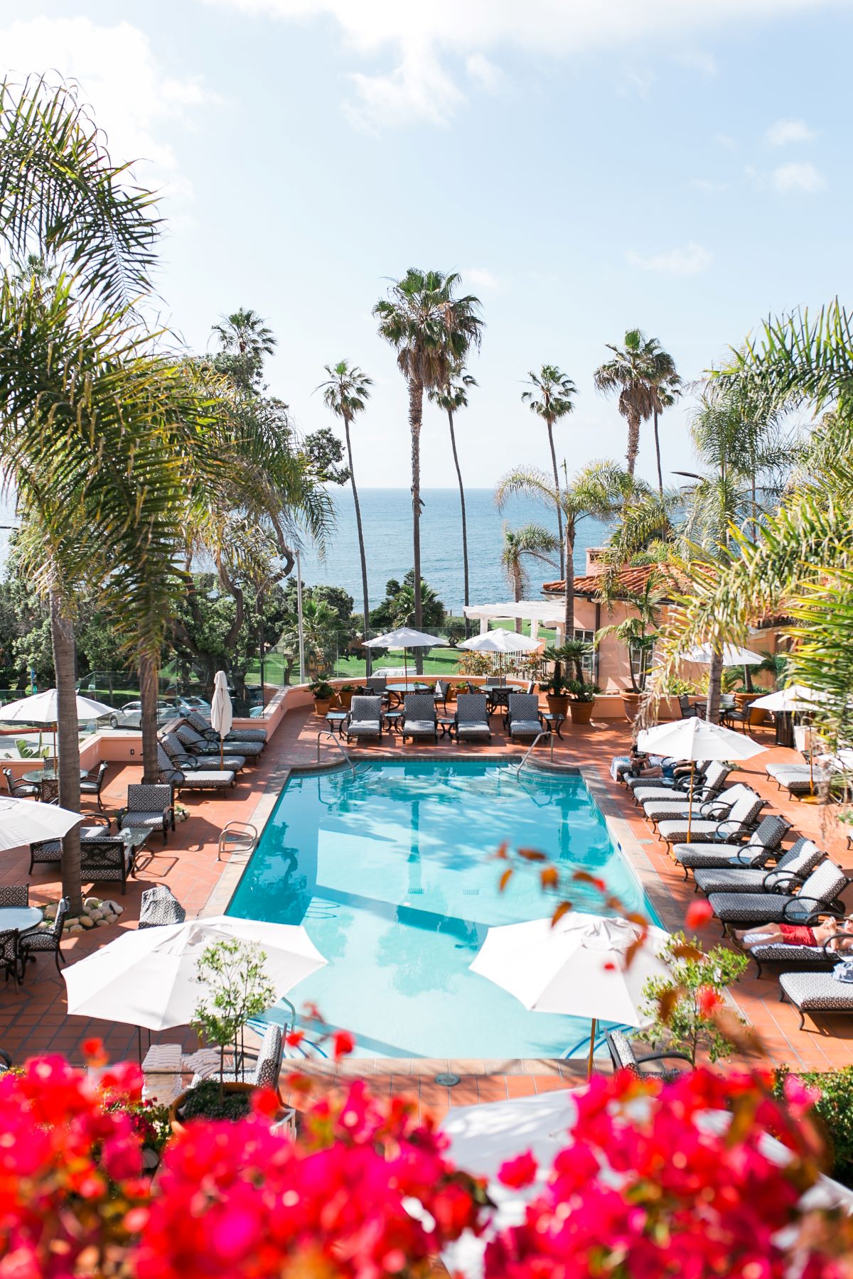 a pool with chairs and umbrellas by a building with palm trees