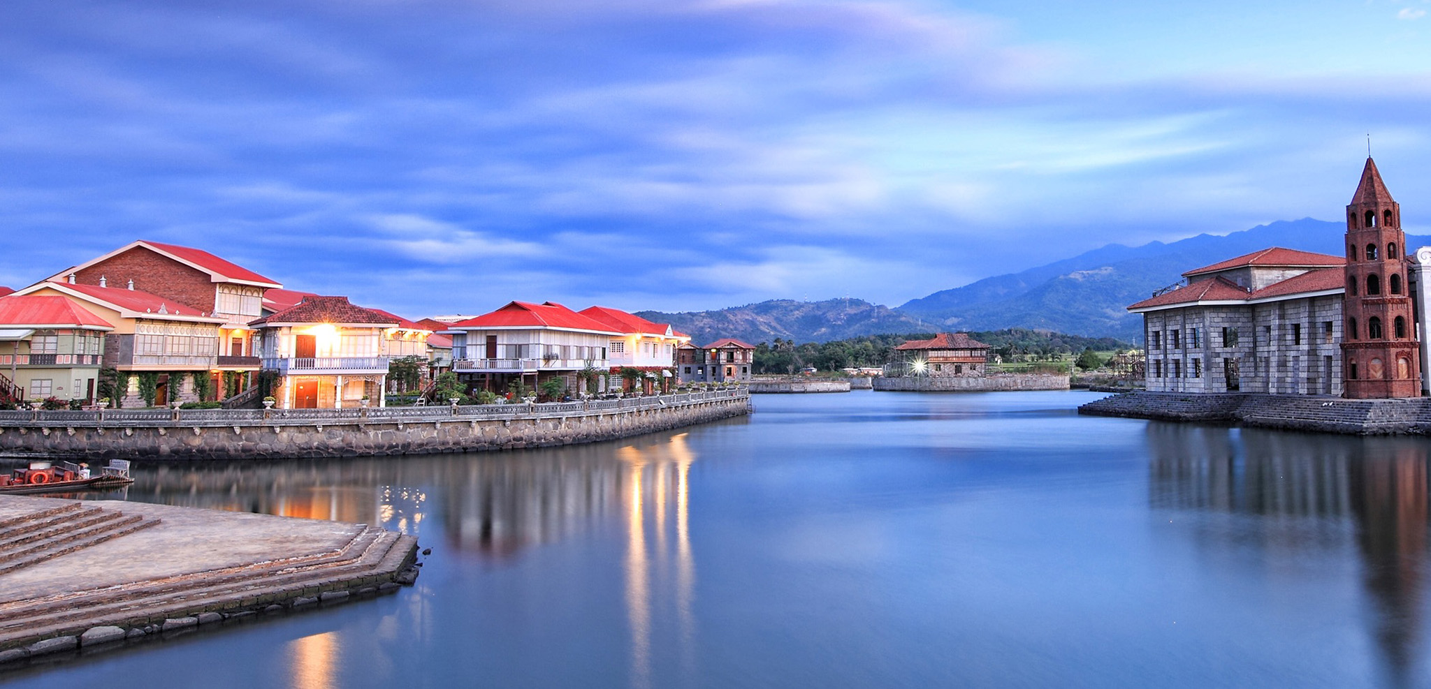 a body of water with buildings and mountains in the background
