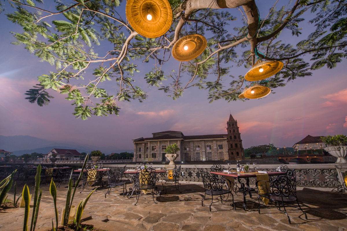 a tree with tables and chairs under a building
