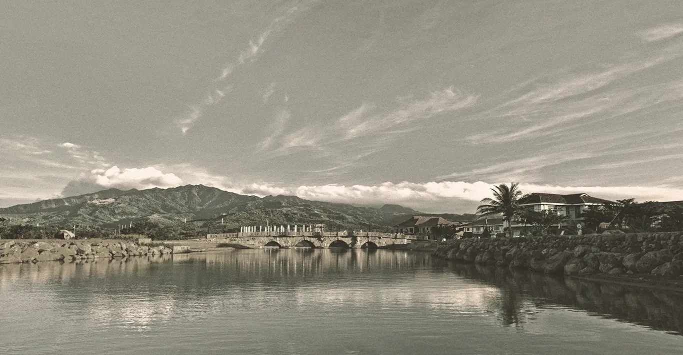 a bridge over water with buildings and mountains in the background