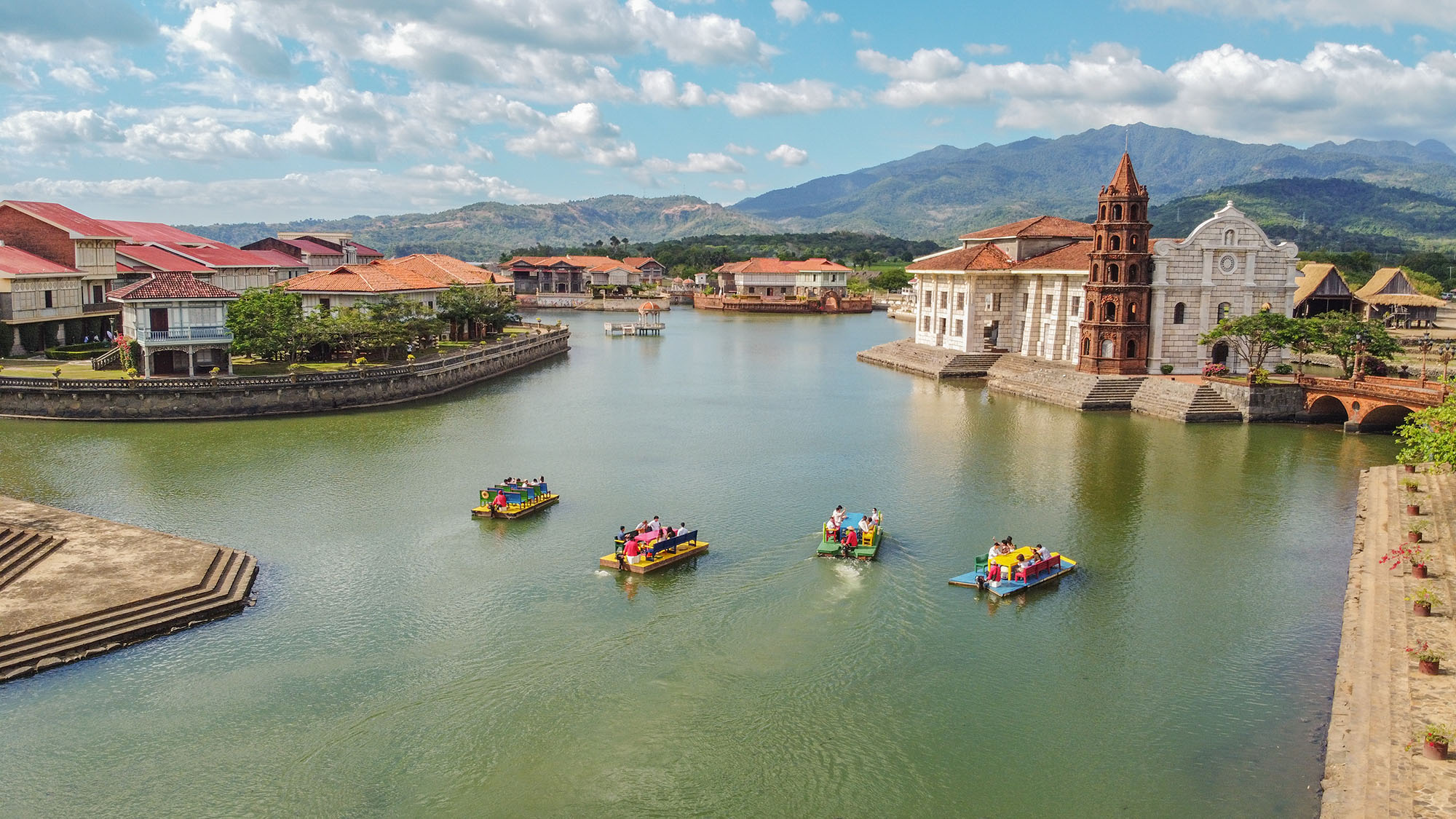 a group of boats in a body of water with buildings and mountains in the background