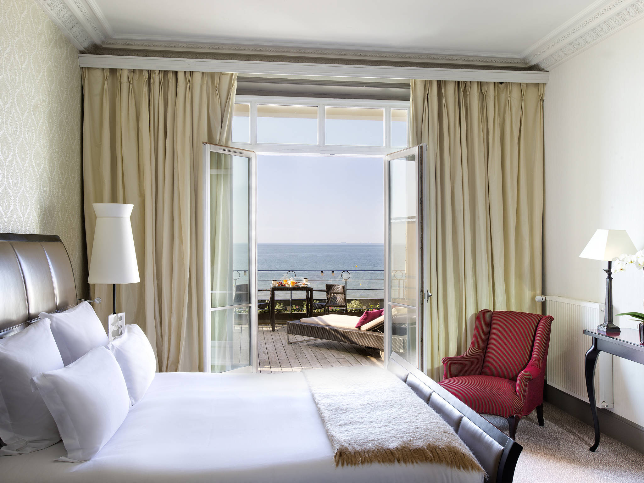 a room with a bed and a chair and a deck with a view of the ocean