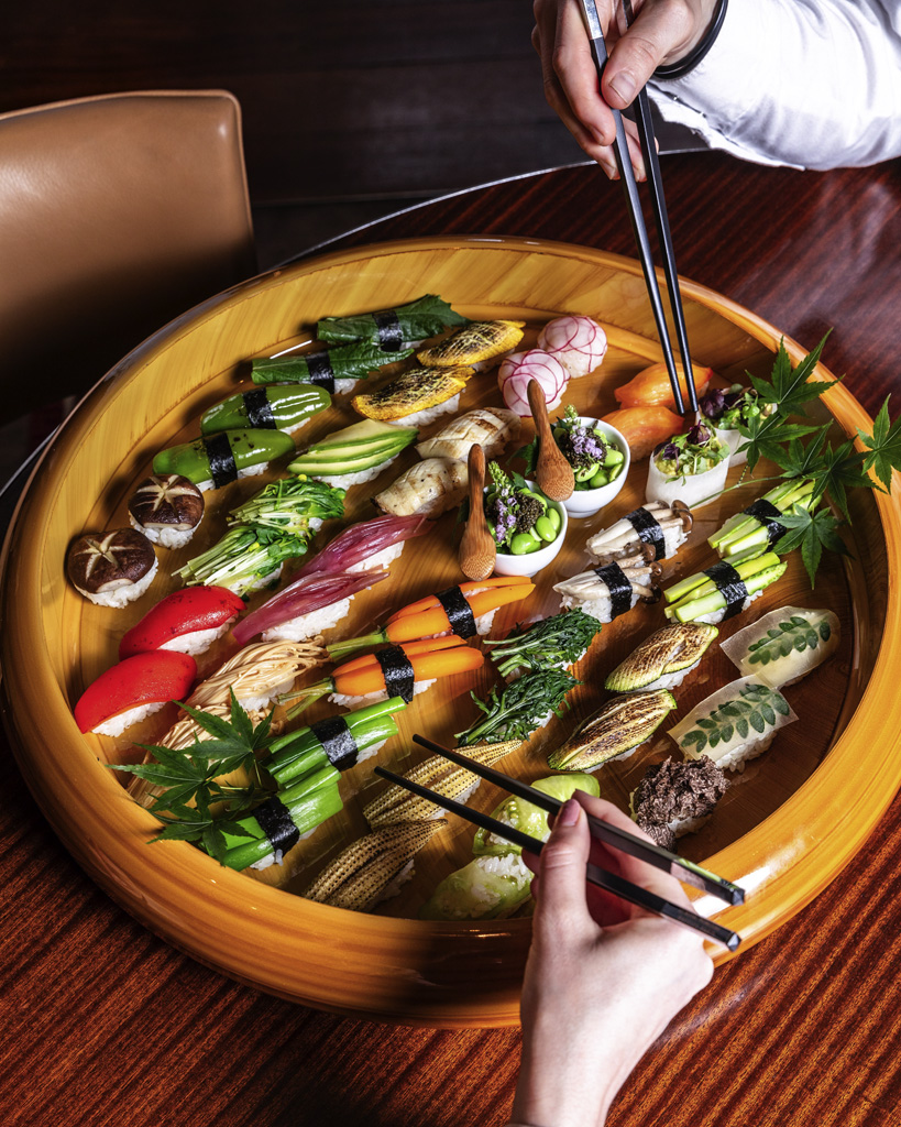 a person holding chopsticks to a plate of sushi