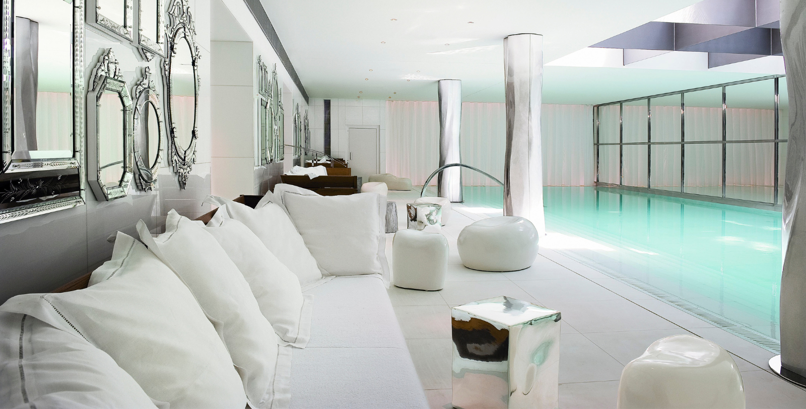 a white couch with white pillows and a pool in the background