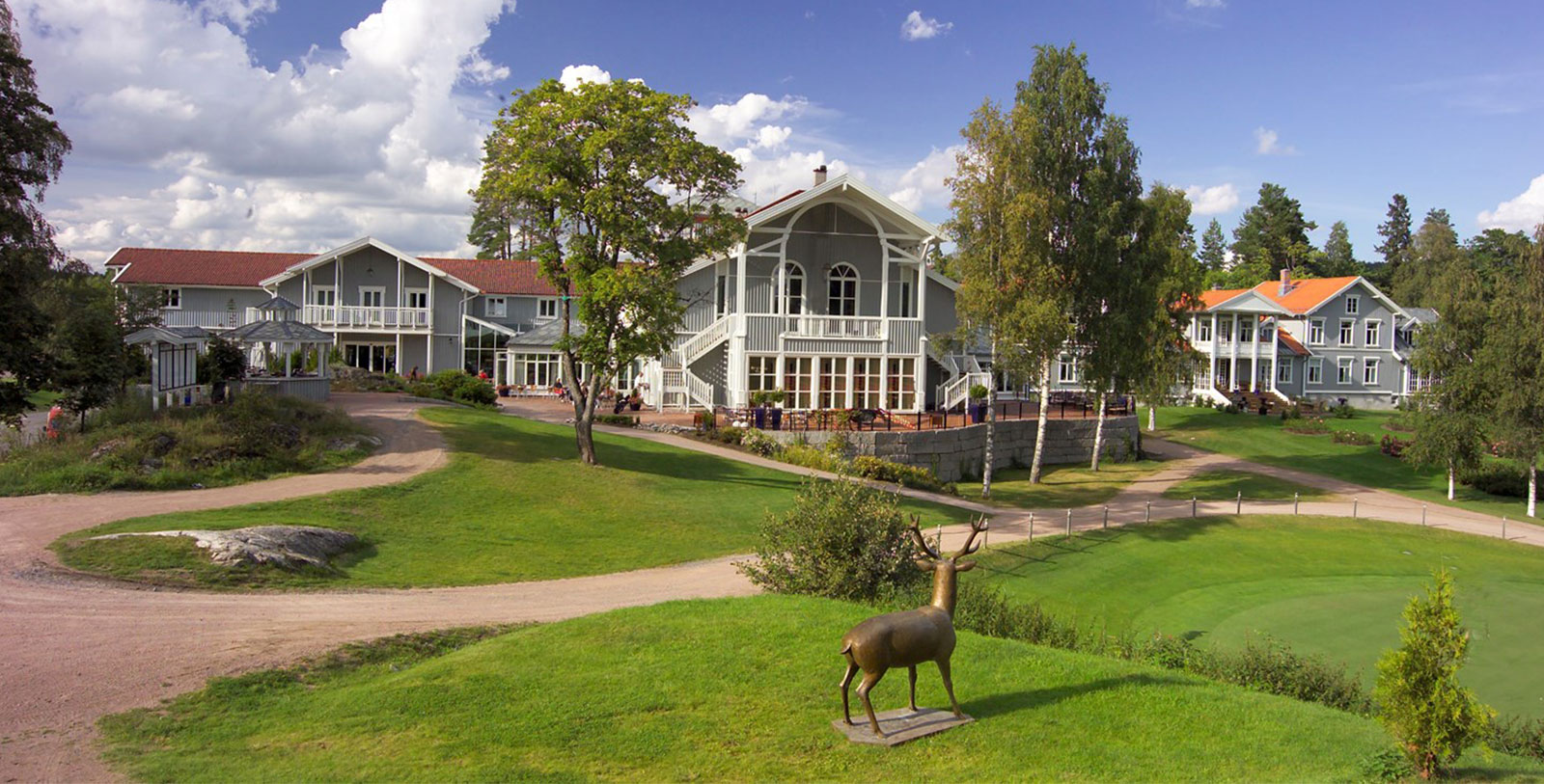a statue of a deer in a grassy area with a large building