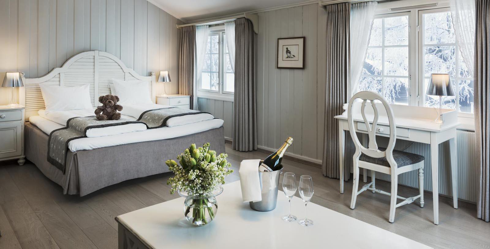 a room with a bed and a table with wine glasses and a vase of flowers