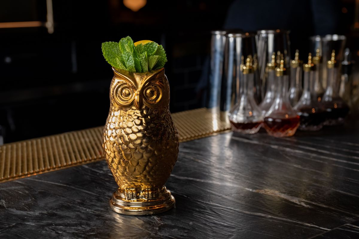 a gold owl shaped drink holder with a lemon and mint leaves