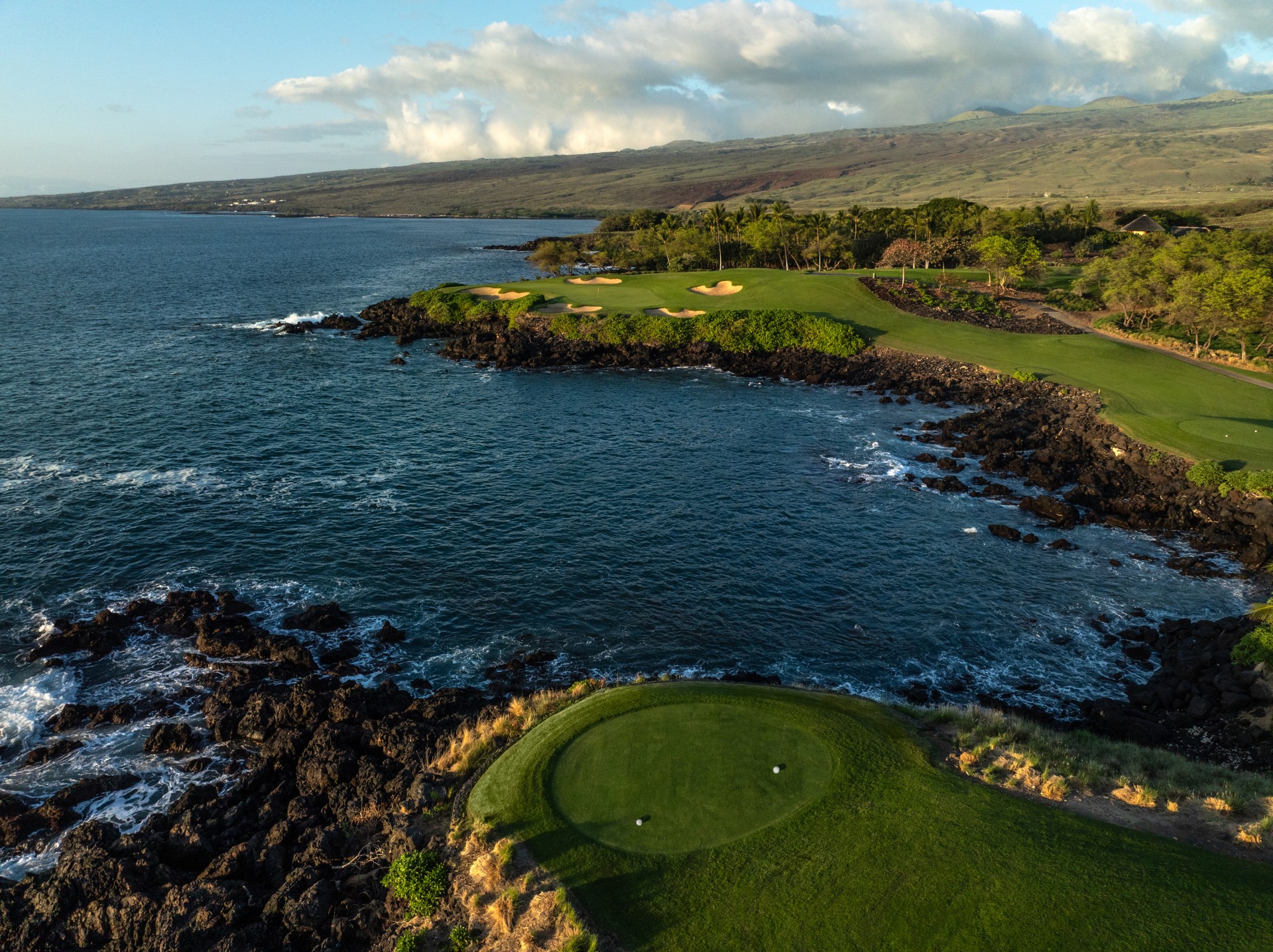 a golf course with a body of water and a hill in the background with Pebble Beach Golf Links in the background