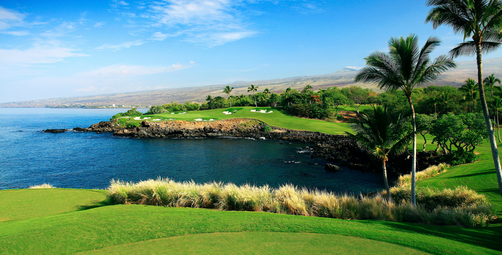 a golf course with a body of water and a mountain in the background