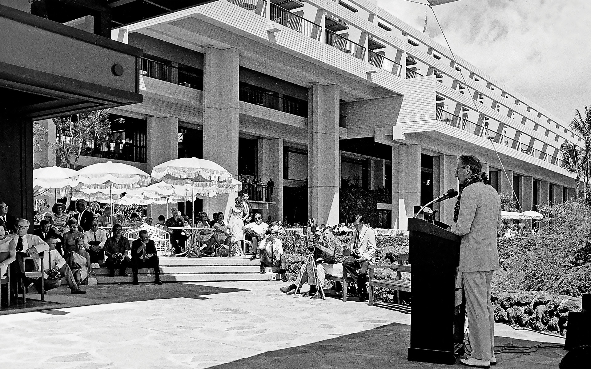 a man standing at a podium with a microphone in front of a building