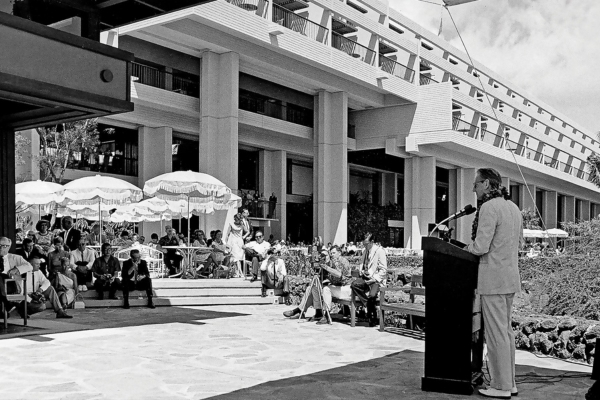 a man standing at a podium with a microphone in front of a building