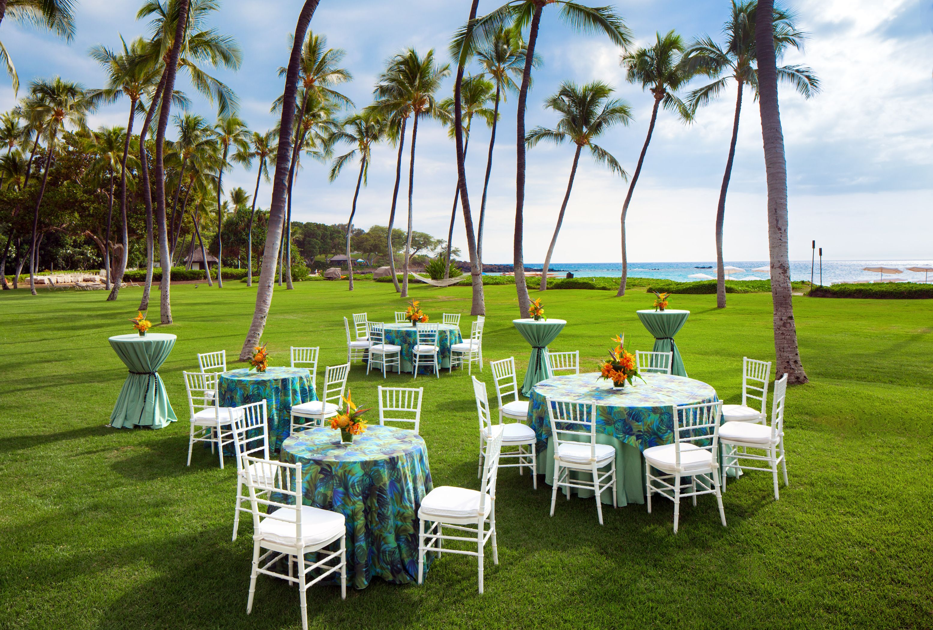 a group of tables and chairs in a grassy area with palm trees