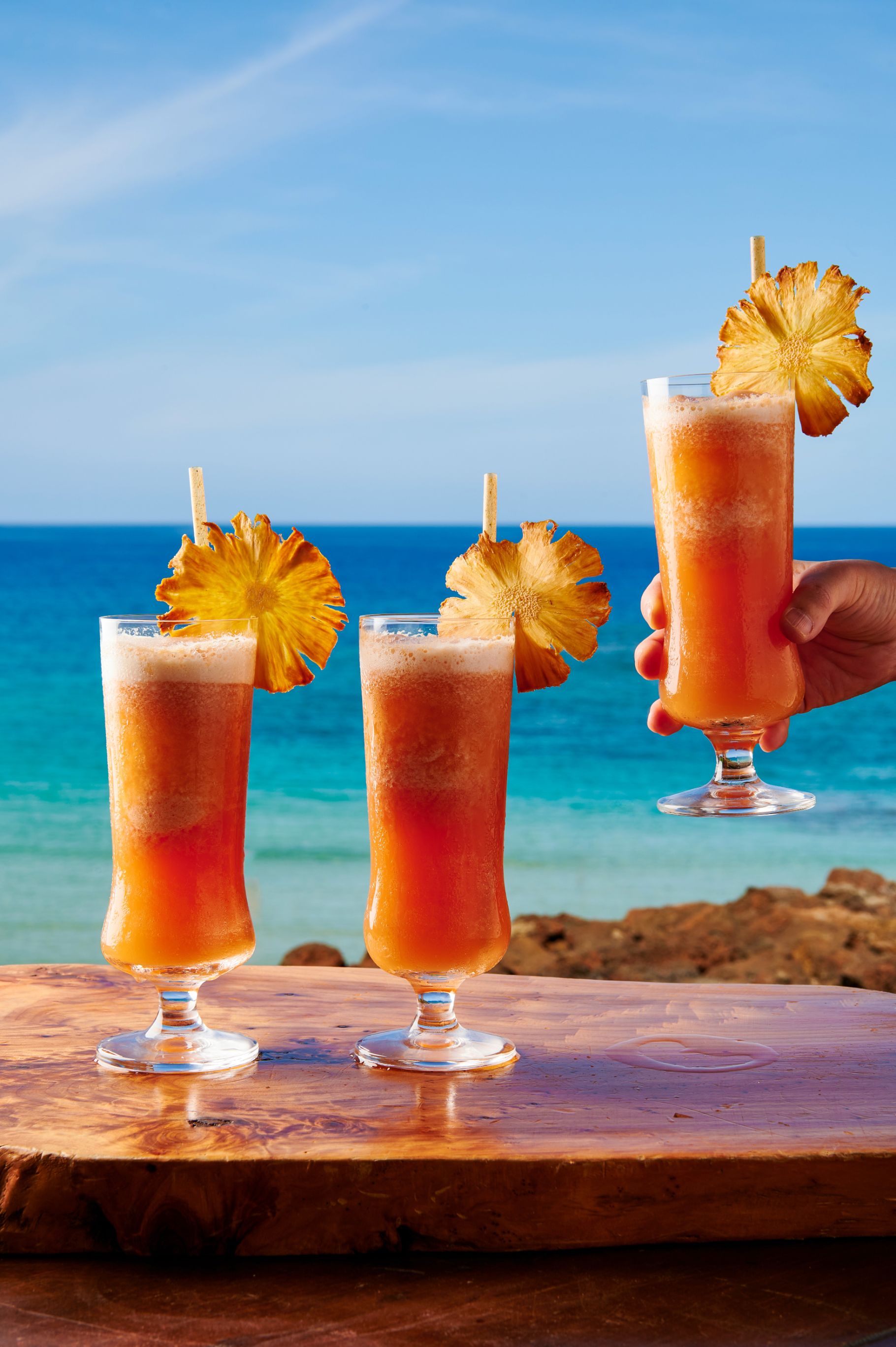 a hand holding a glass of drink with a pineapple on top