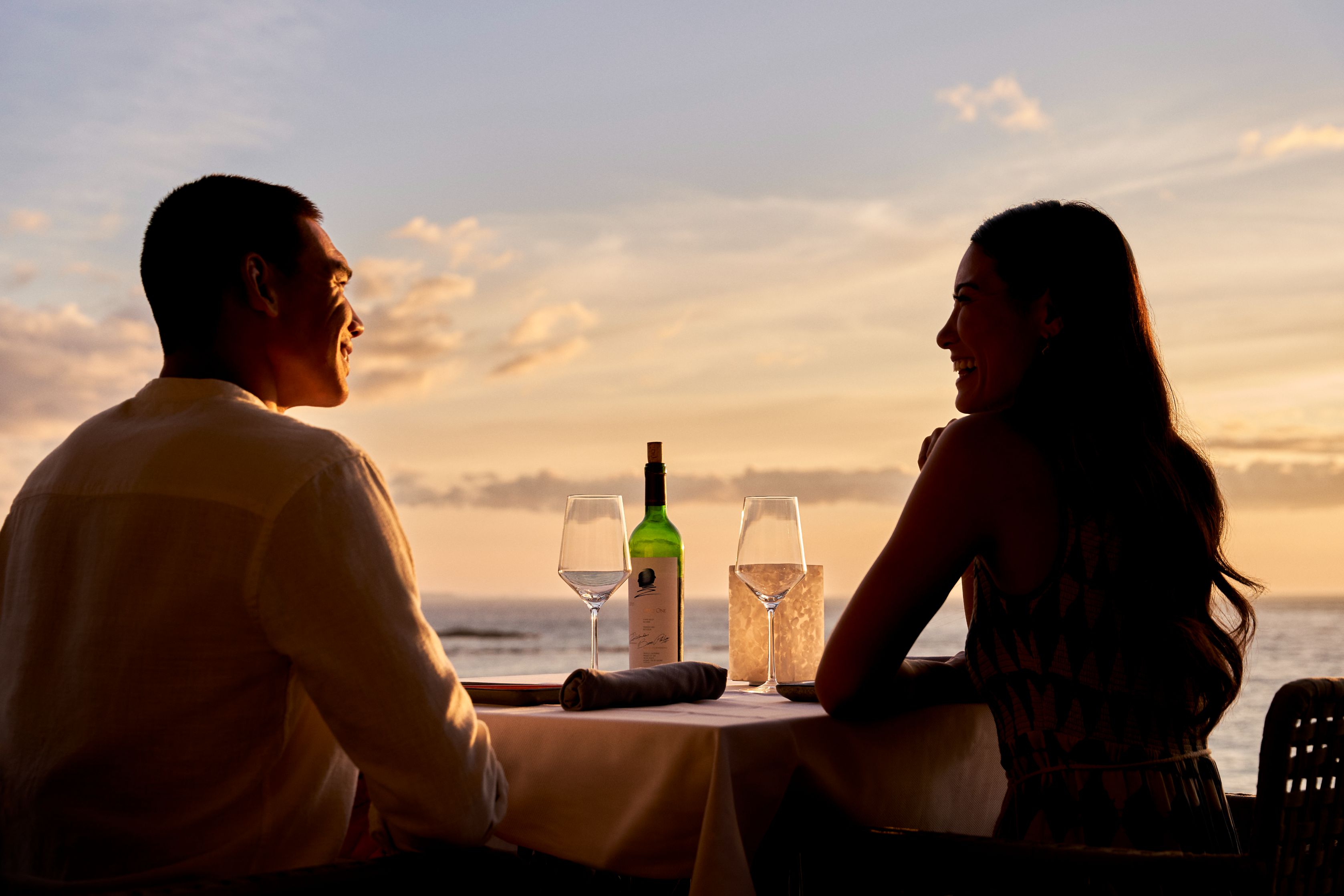 a man and woman sitting at a table with wine glasses and a bottle of wine