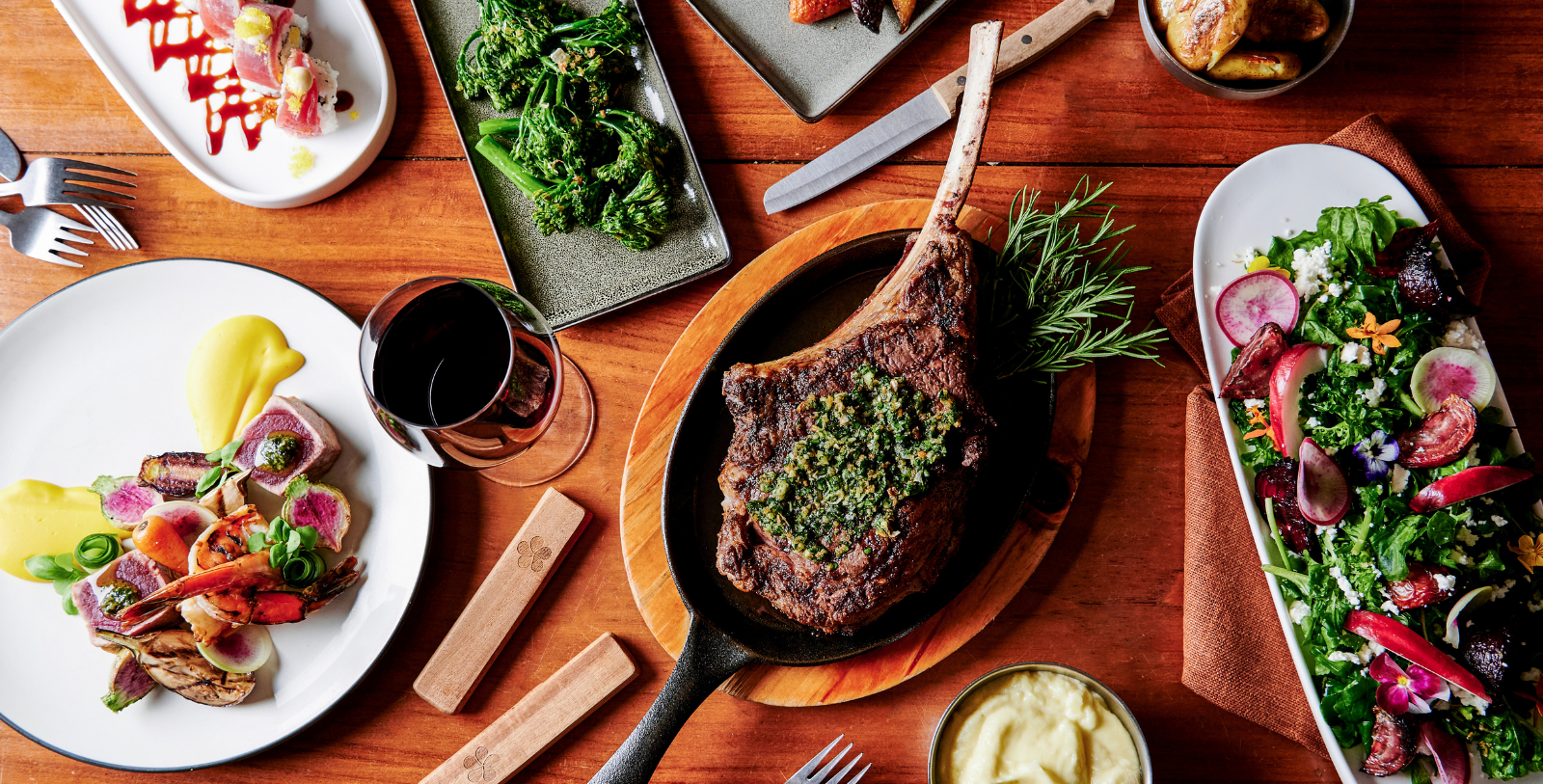 a steak on a pan with a side of vegetables and a glass of wine