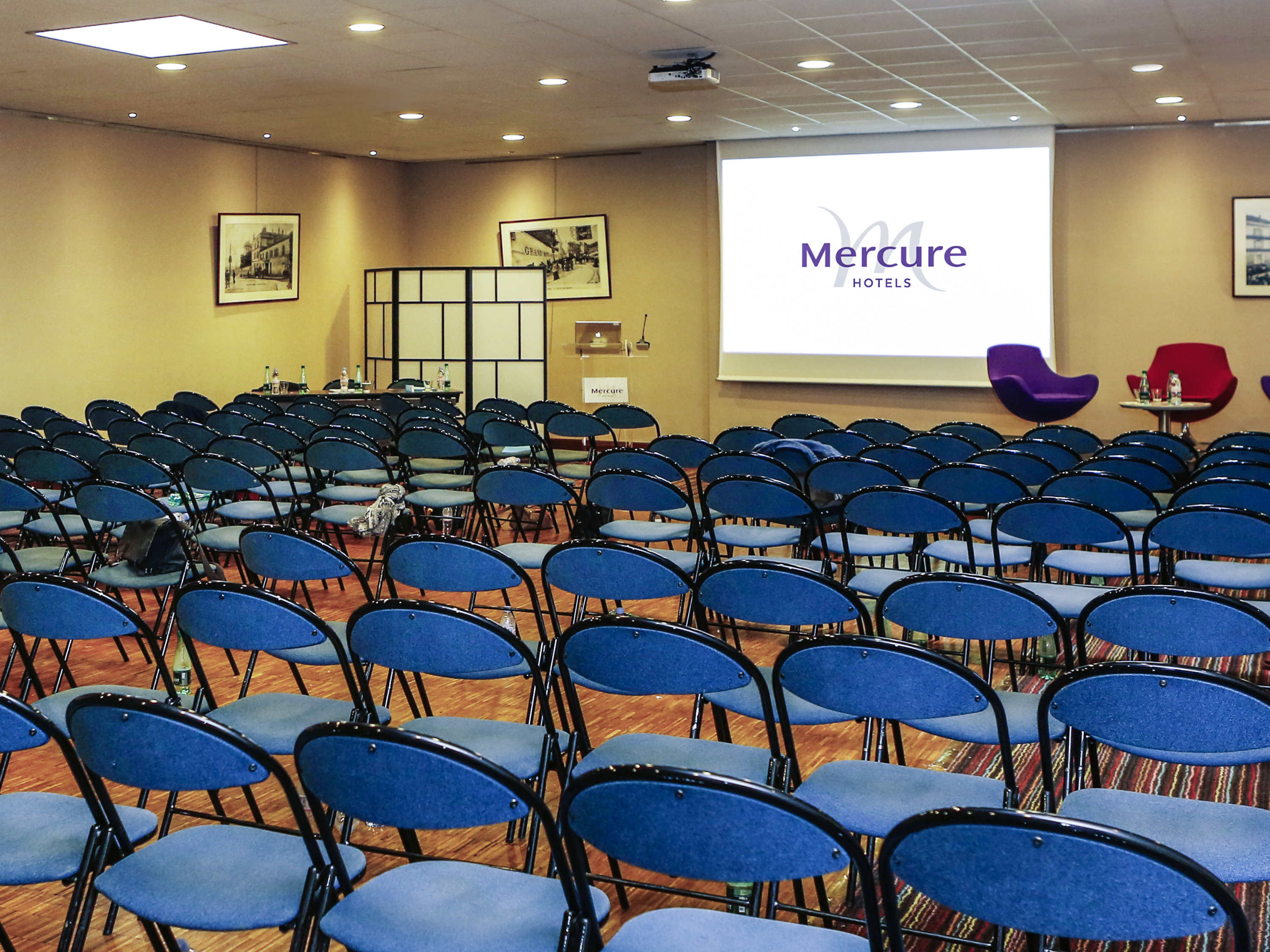 a room with rows of blue chairs and a projector screen