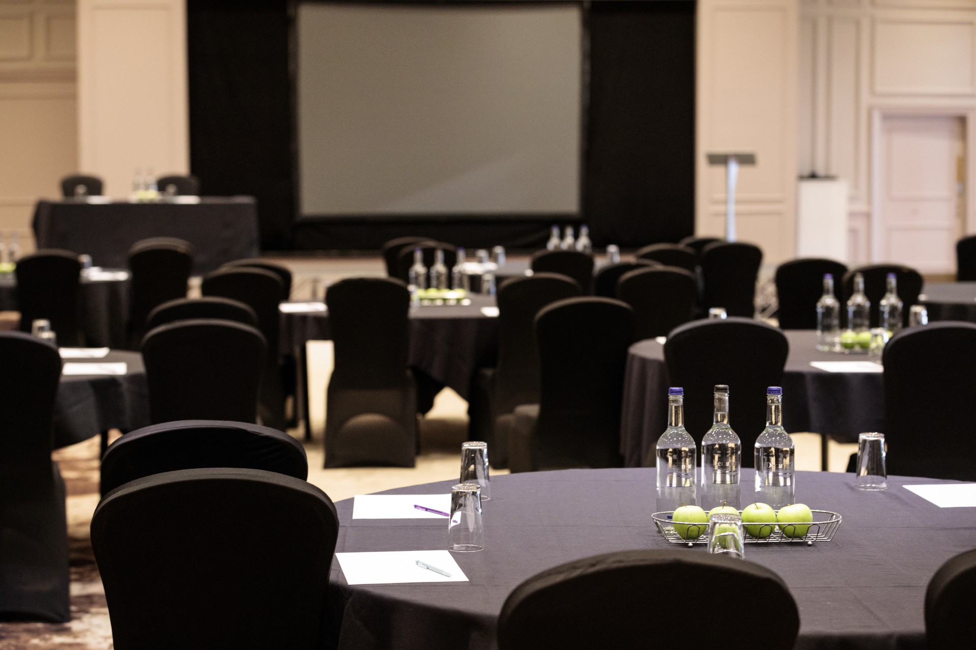 a room with black chairs and a table with black tablecloths and a screen