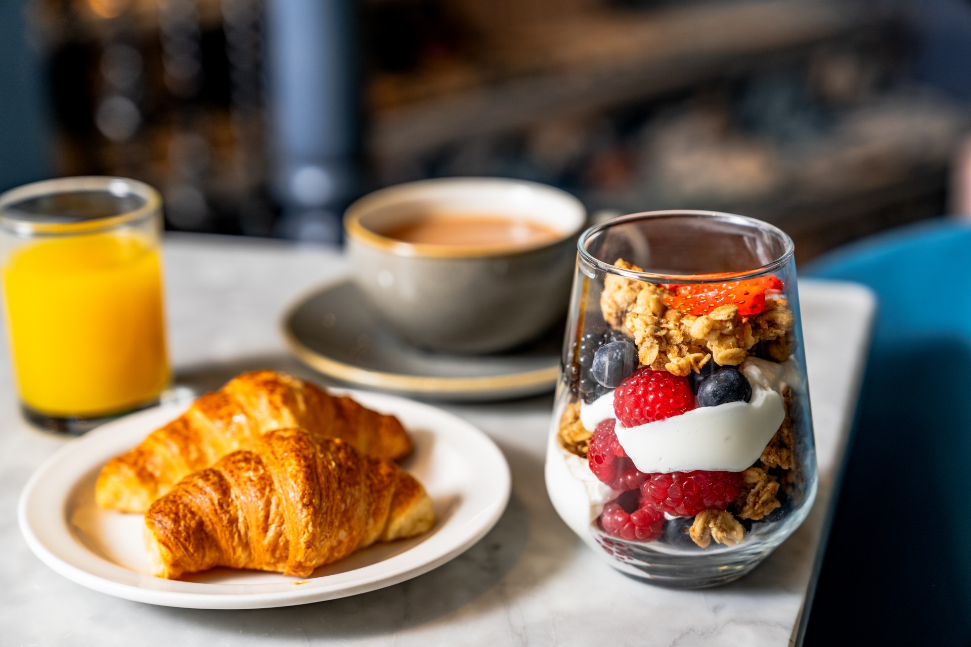 a glass of fruit parfait and croissants on a table