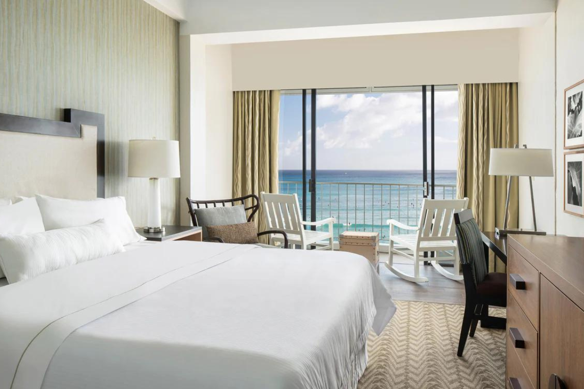 a room with a bed and chairs and a large window overlooking the ocean