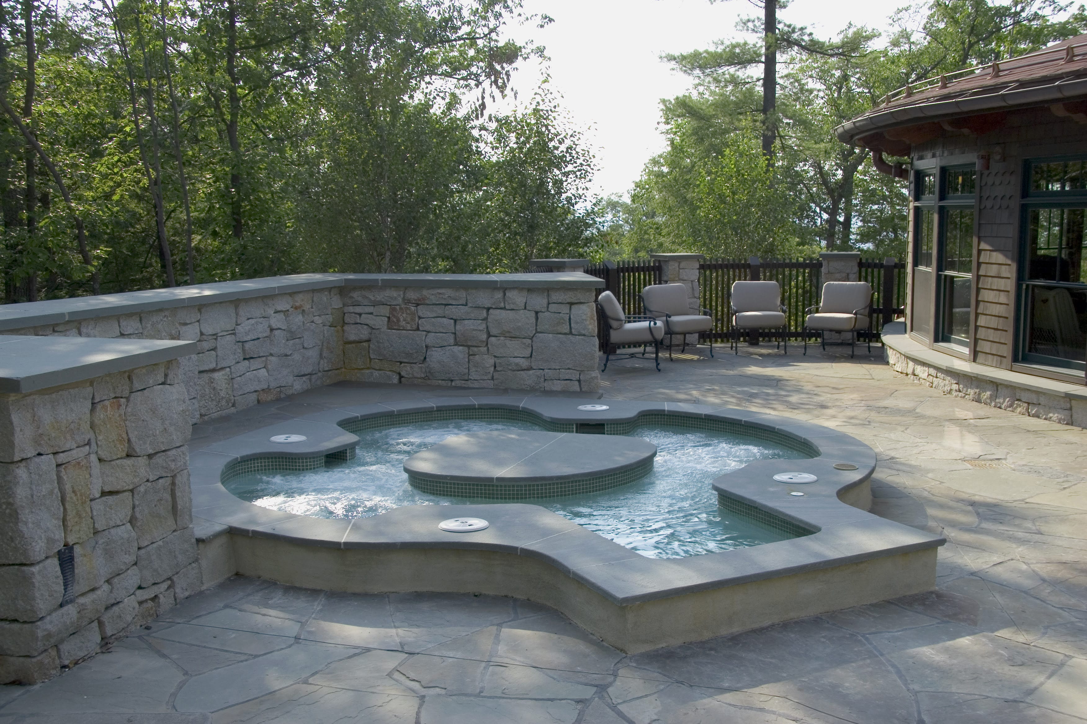 a hot tub with a stone wall and chairs