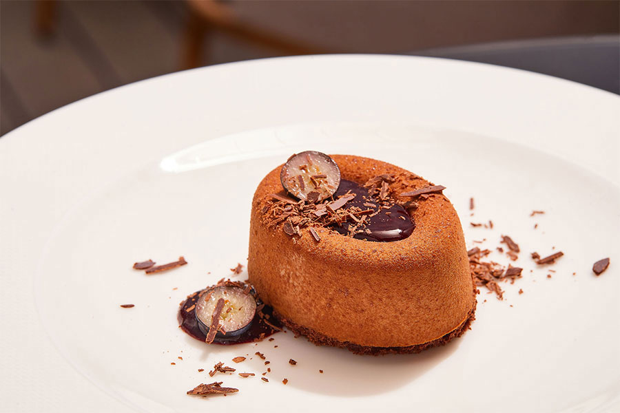 A gourmet chocolate lava cake dessert garnished with chocolate shavings, blueberry sauce, and halved fresh blueberries, presented on a white porcelain plate.