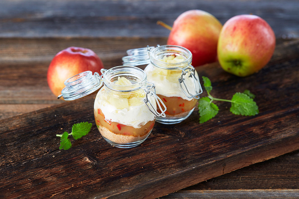 a jar of dessert with apples on a wood surface