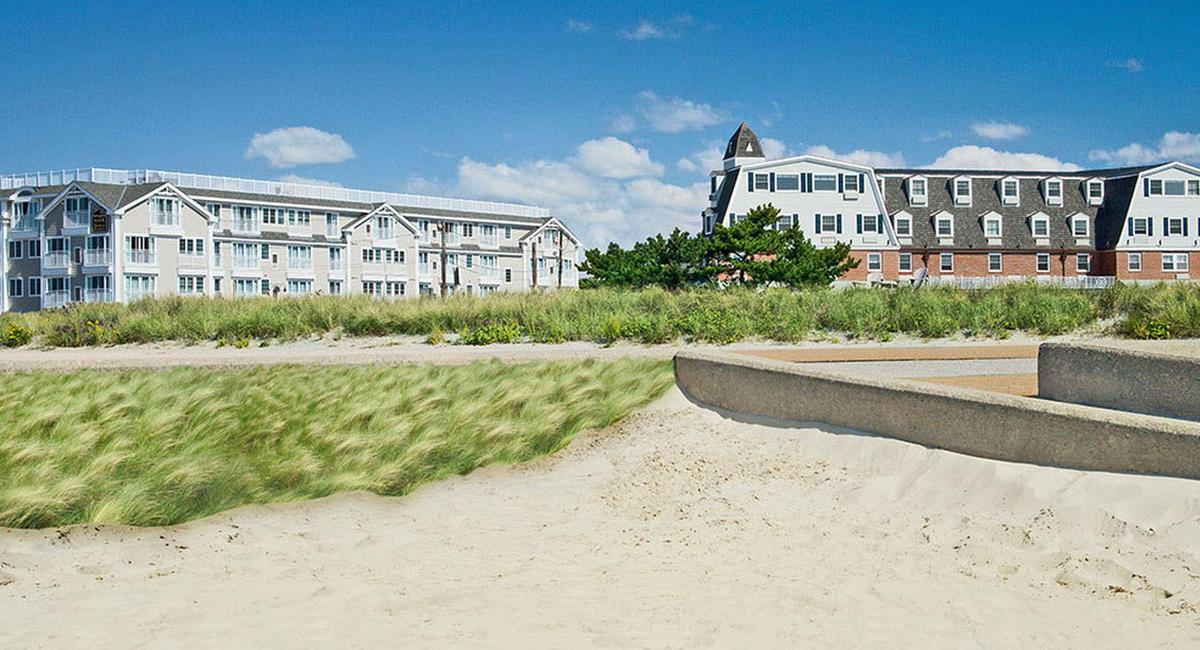 a sand dune with a concrete wall and a grassy area with buildings in the background