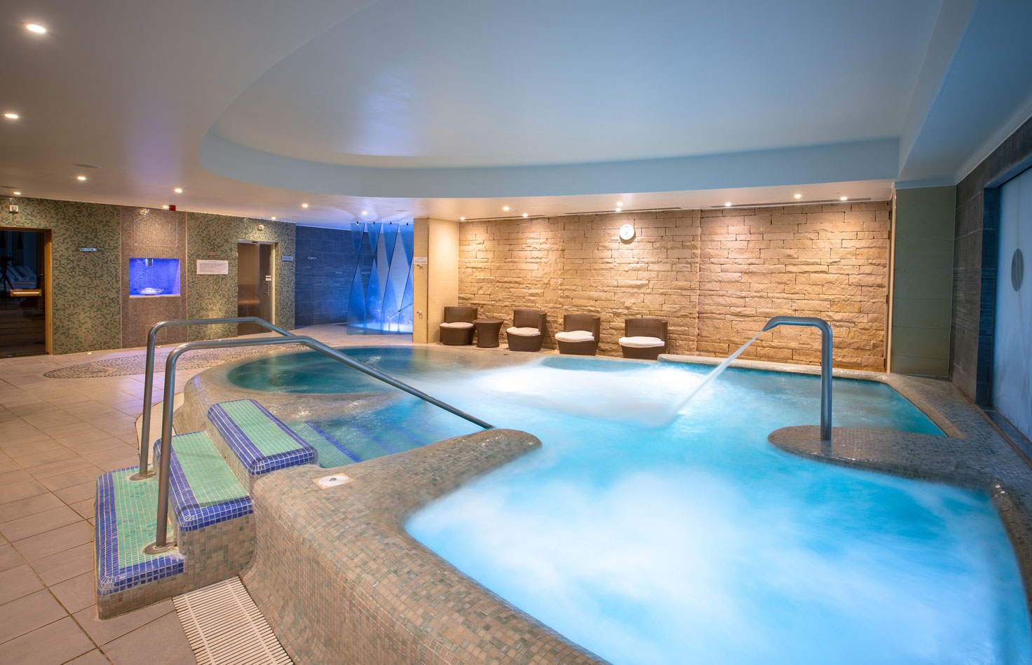 a large indoor pool with a large tub and a stone wall