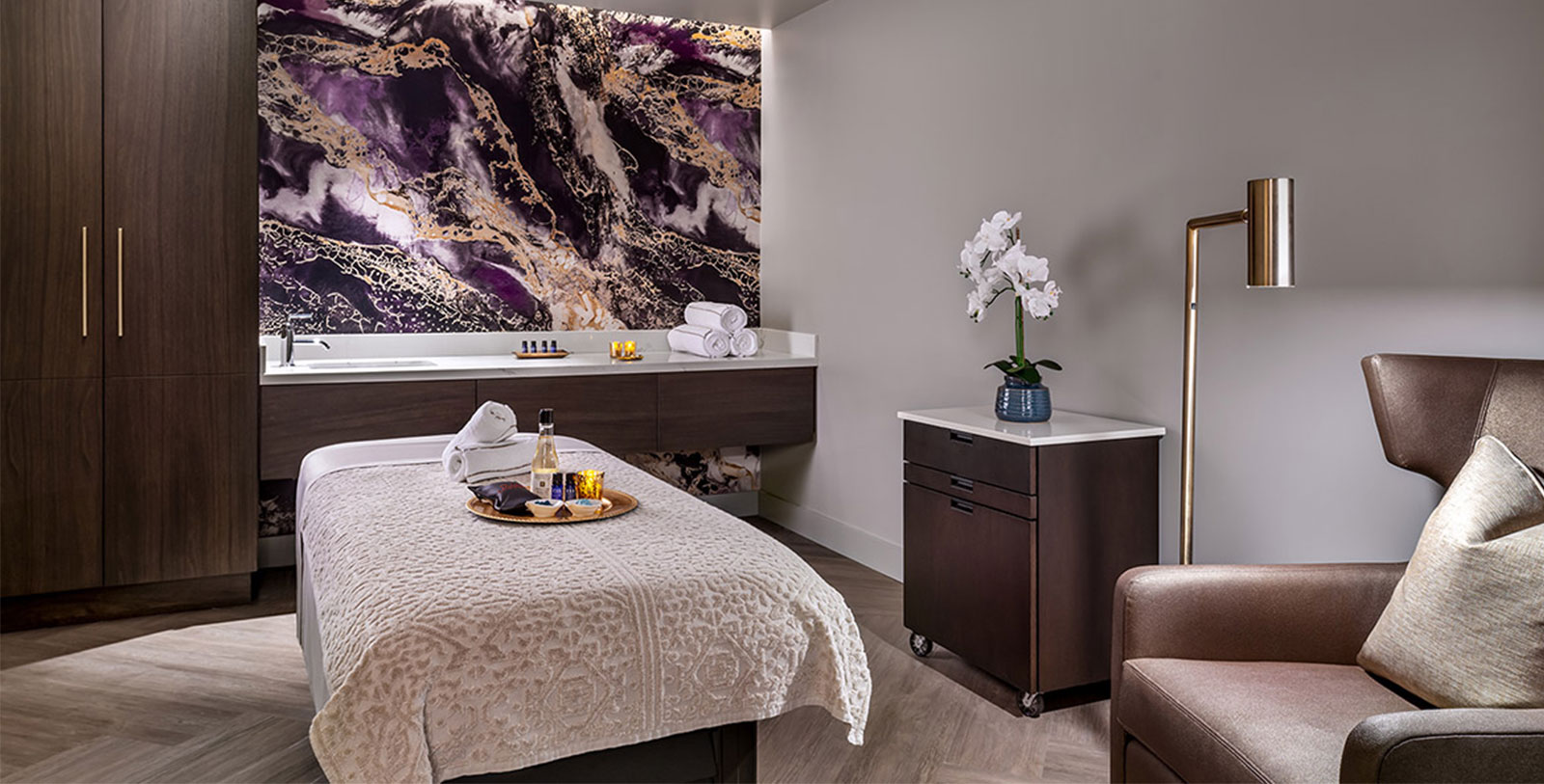 a room with a bed and a table with towels and a vase of flowers