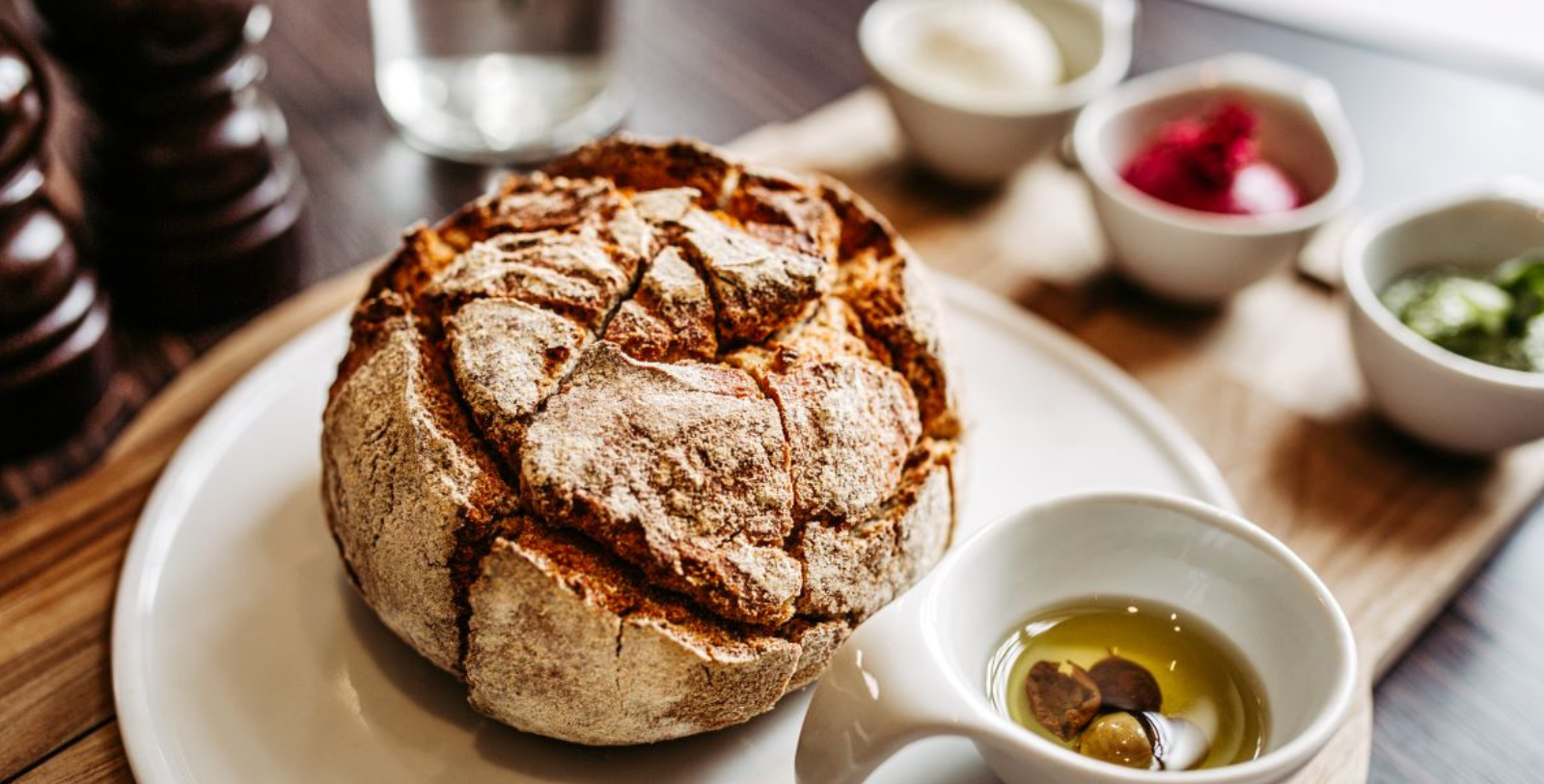 a round loaf of bread with olives and a small white bowl of oil