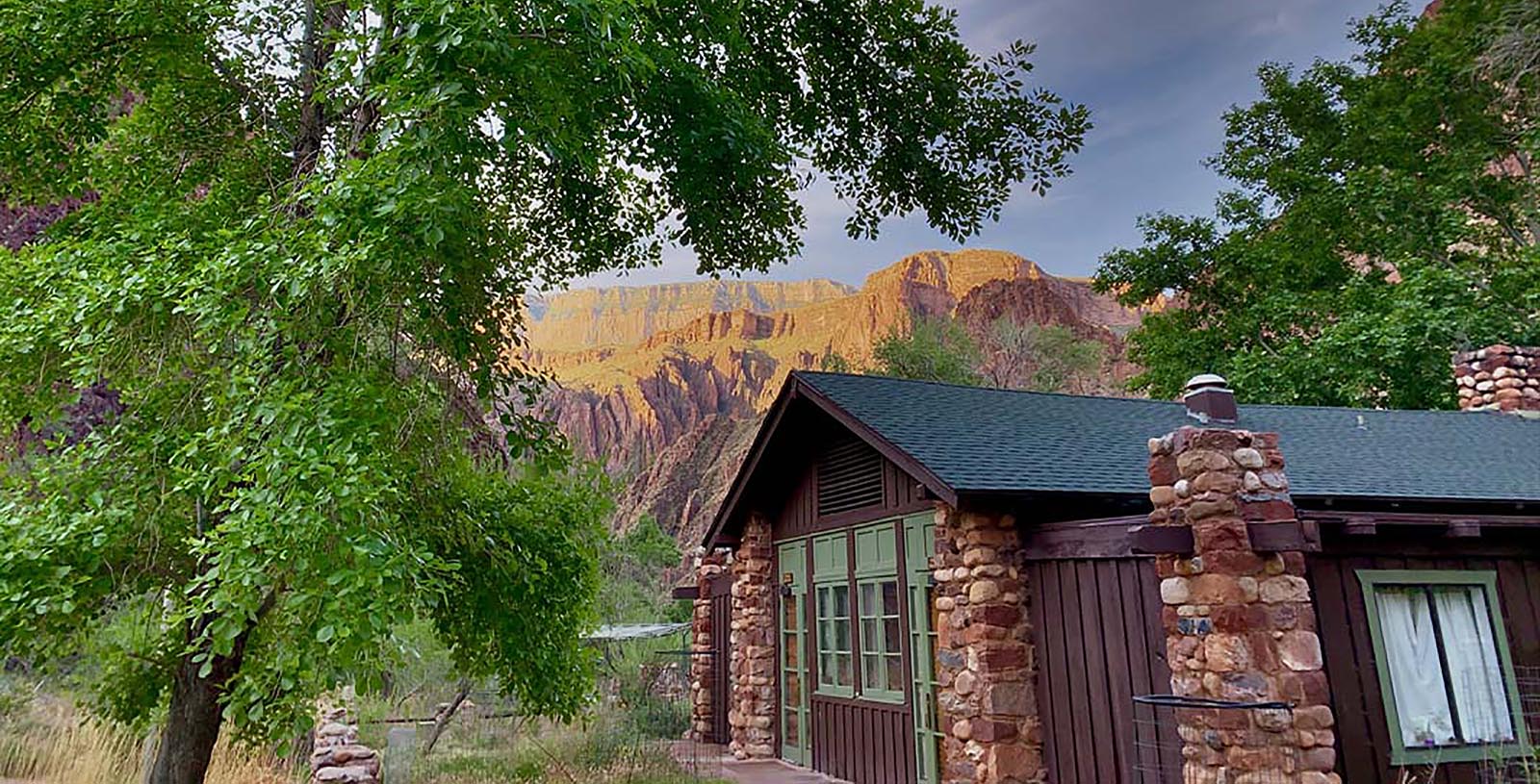 a house with a stone wall and a tree in front of a mountain