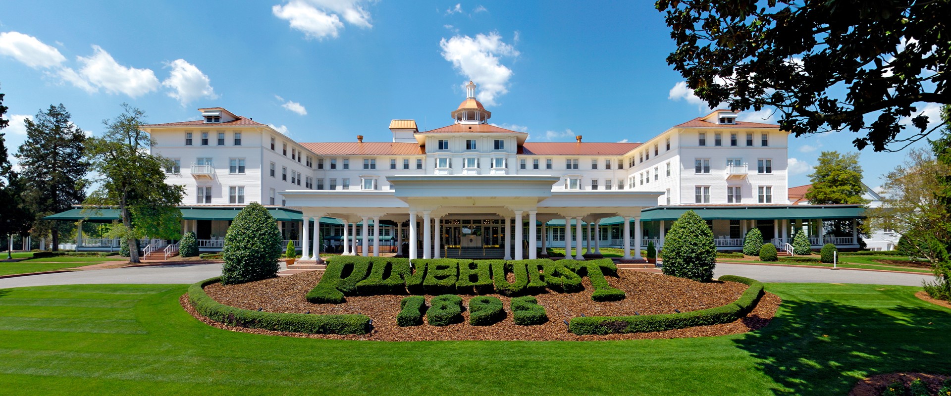 a large white building with columns and a sign in front of it with Pinehurst Resort in the background