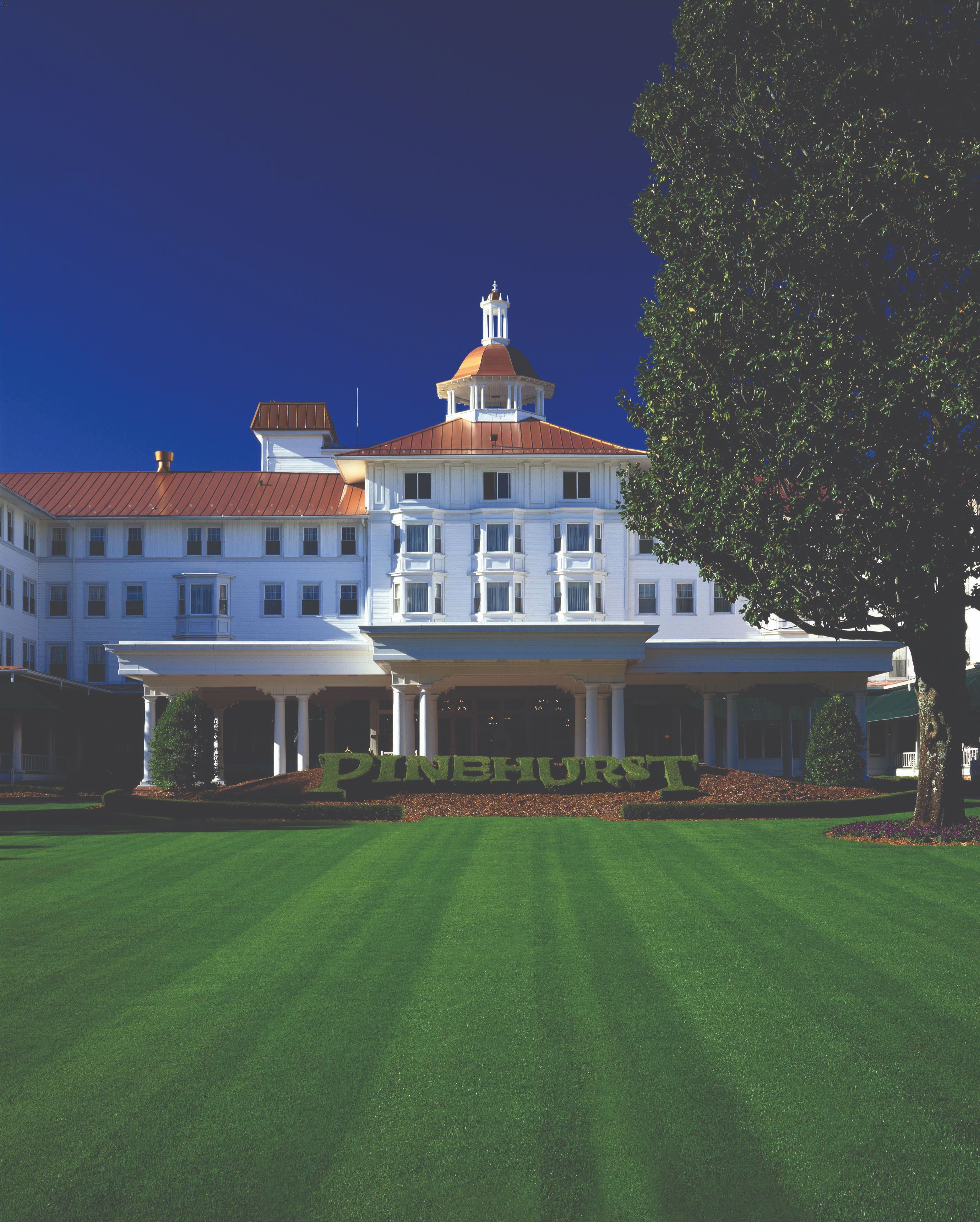 a large white building with a lawn and a tree with Pinehurst Resort in the background