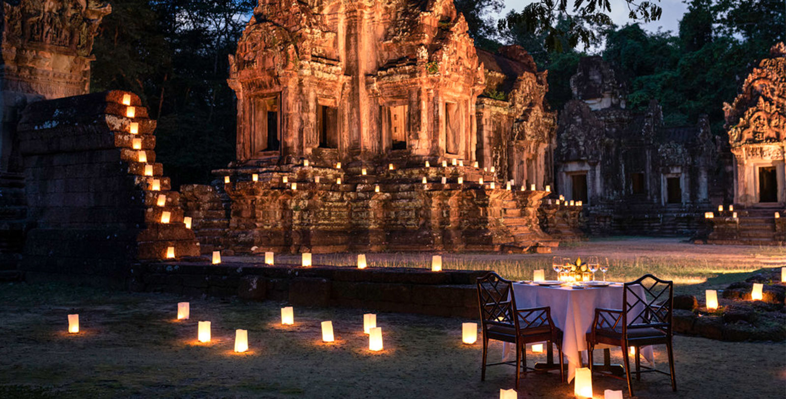 a table set up for a dinner with candles in front of a stone building