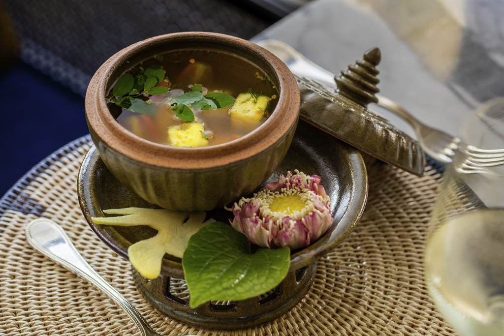 a bowl of soup with a lid and a flower on a plate