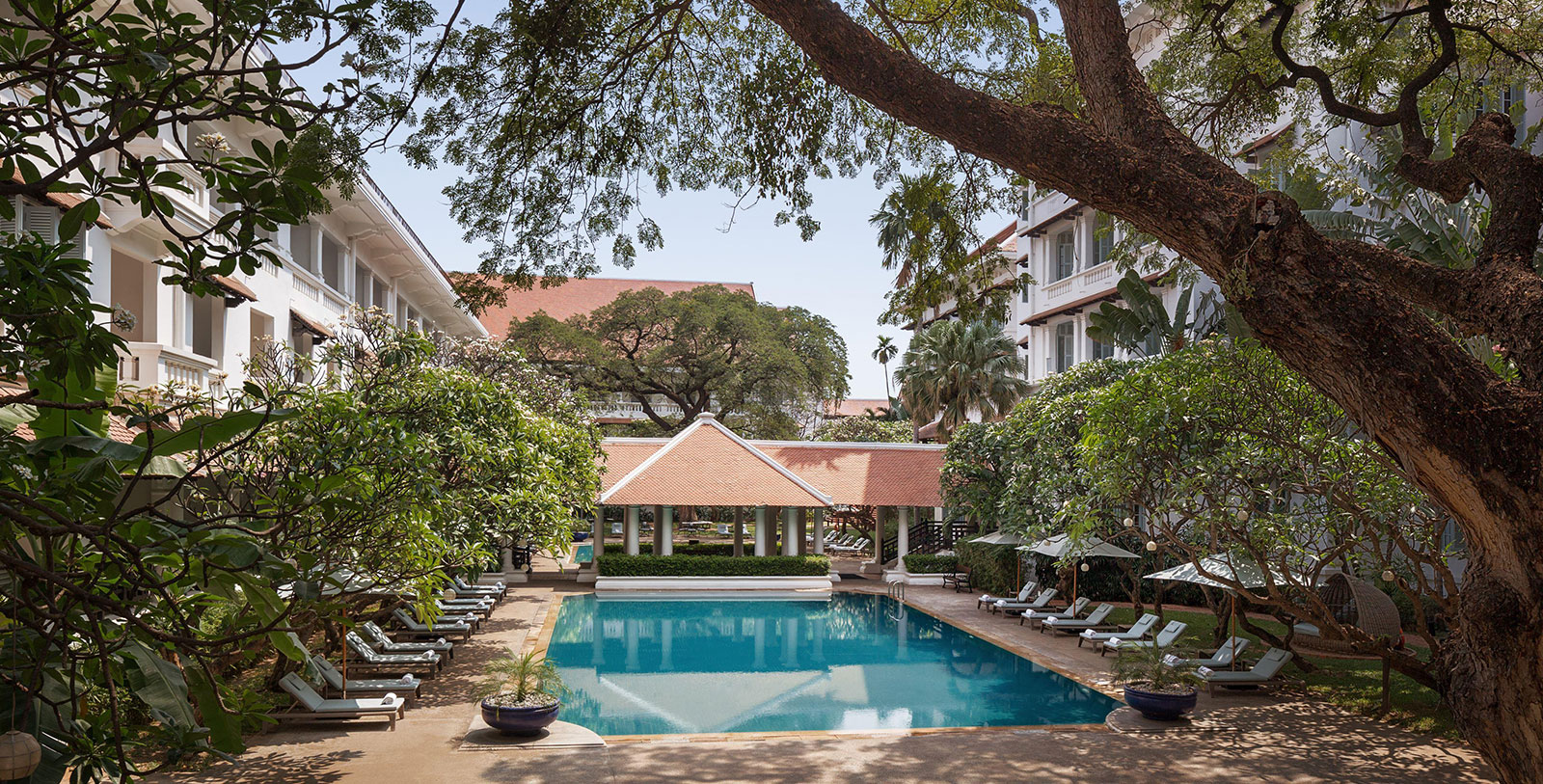 a swimming pool with lounge chairs and trees around it