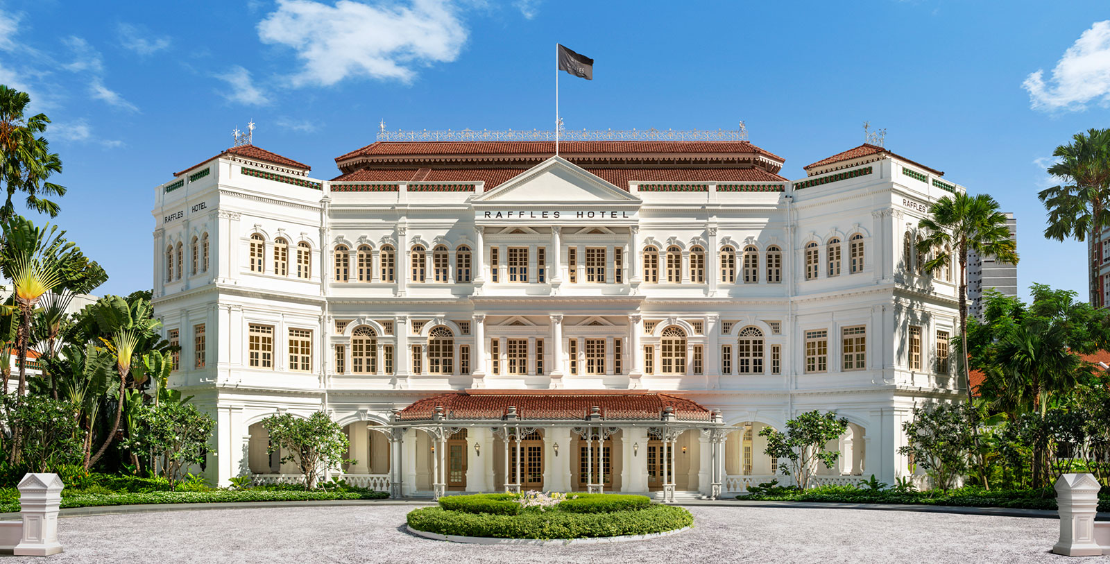 a white building with a flag on top with Raffles Hotel in the background