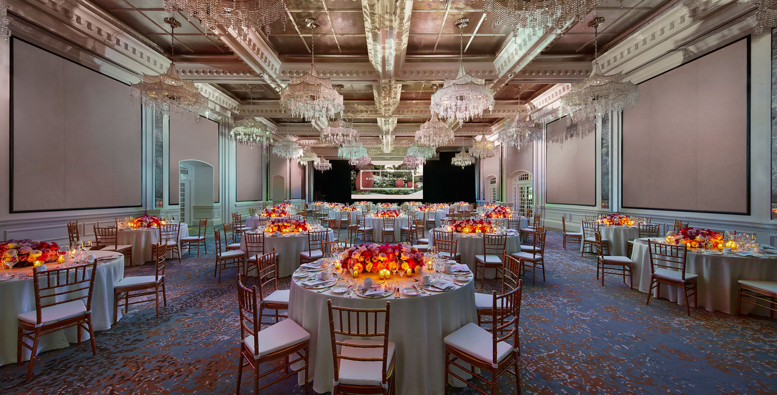a room with tables and chairs with flowers and chandeliers