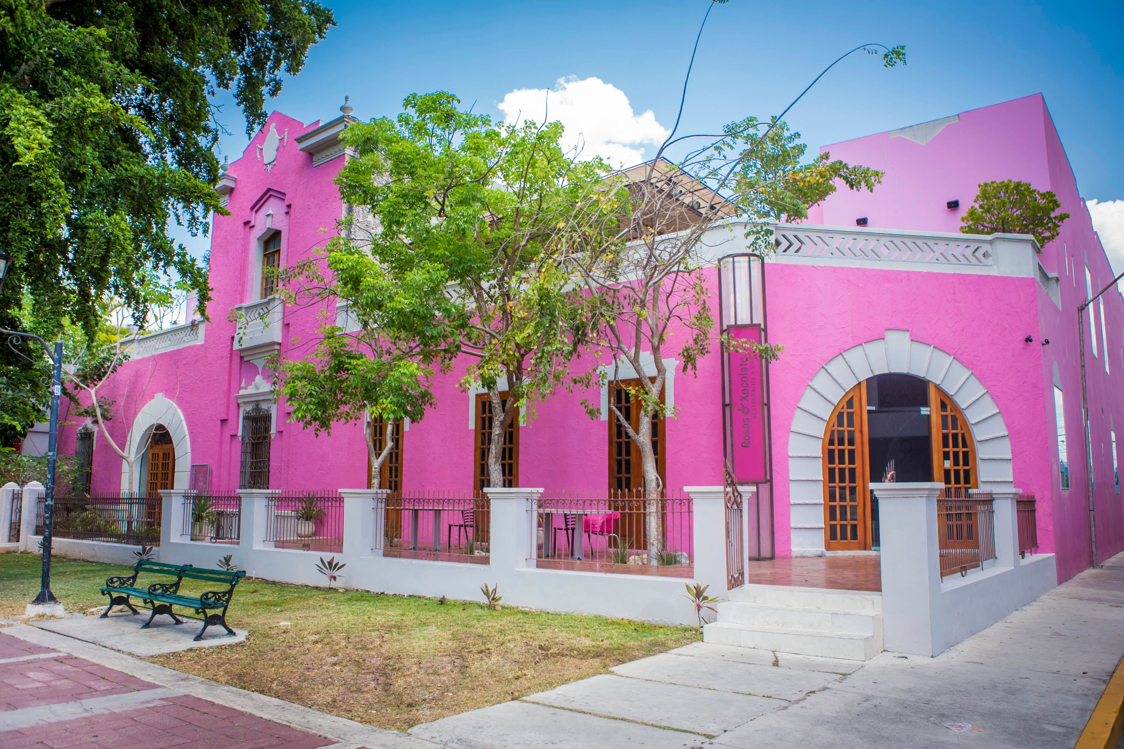 a pink building with a white railing and a bench