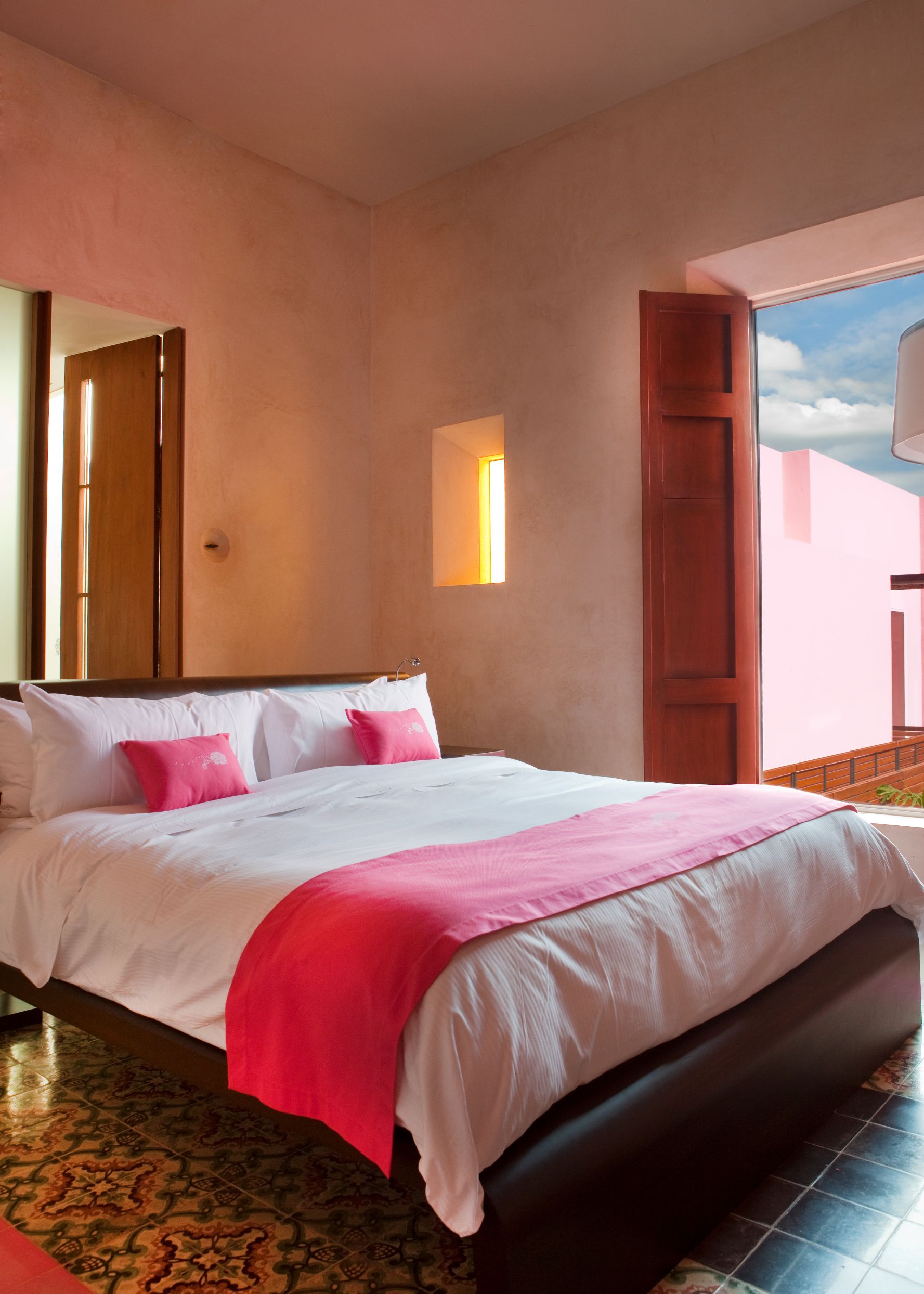 a bed with pink pillows and a lamp in a room with a window