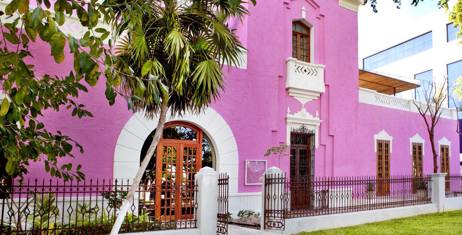a pink building with a fence and palm tree
