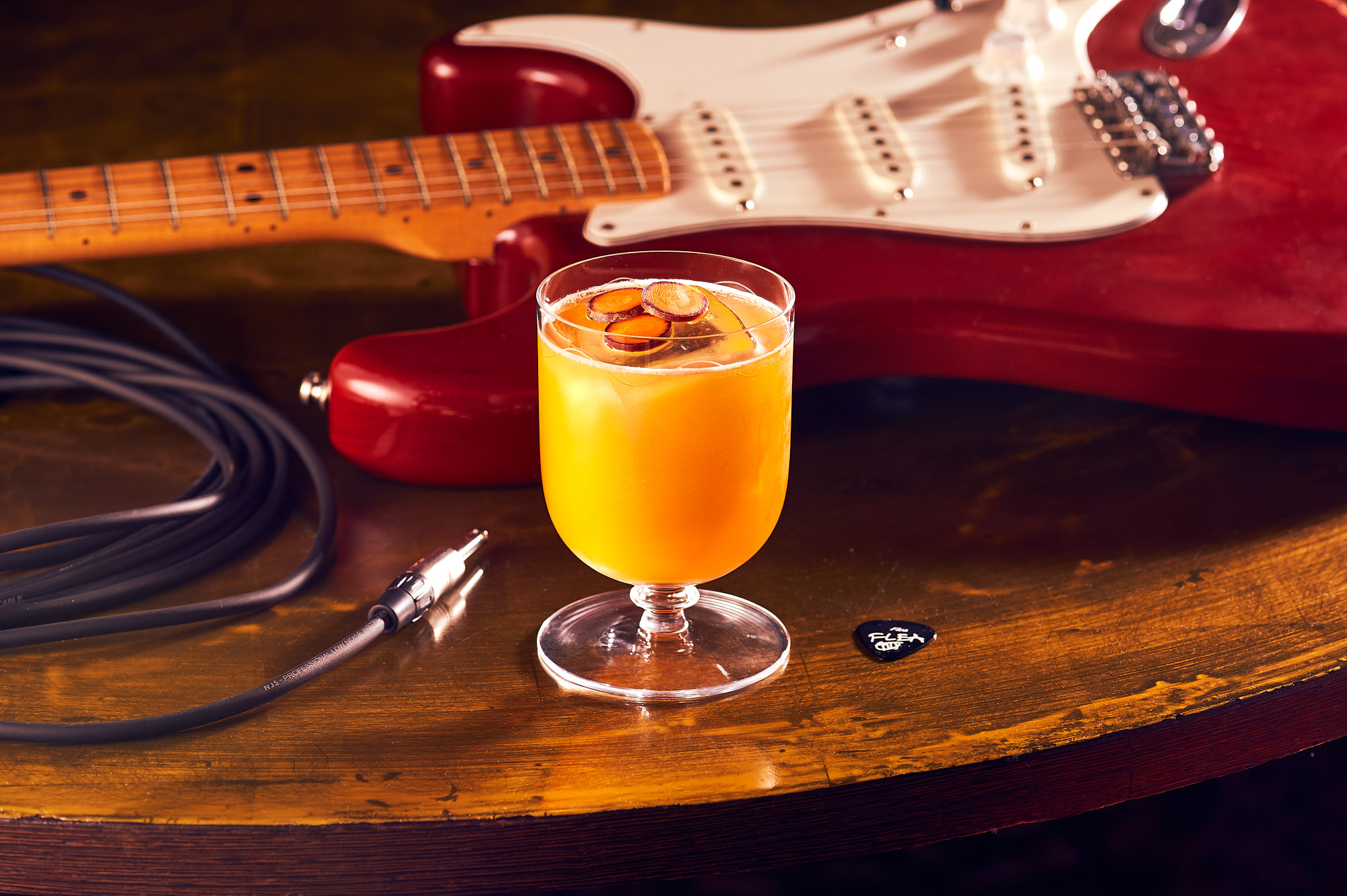 a glass of orange liquid next to a guitar