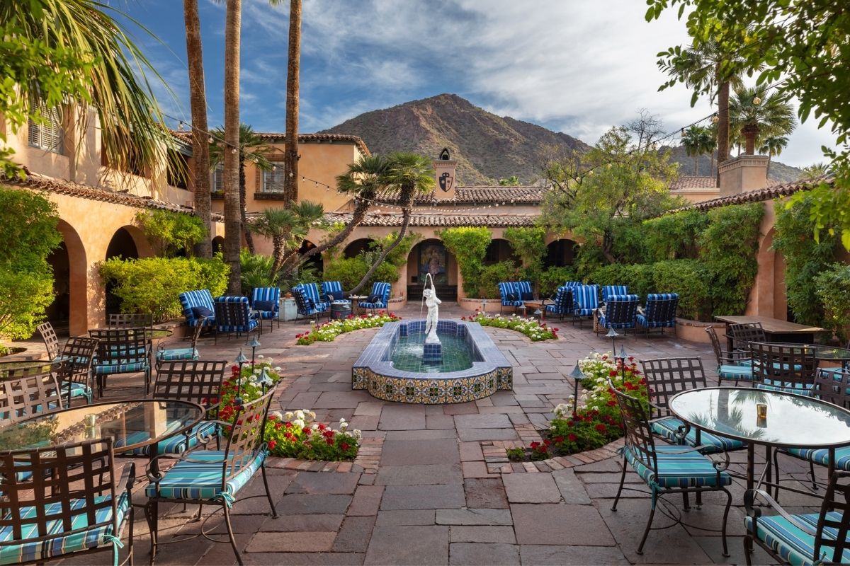 a courtyard with a fountain and chairs and a mountain in the background