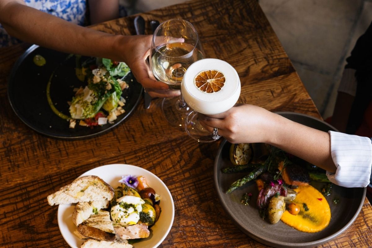 a person holding glasses of wine and a plate of food